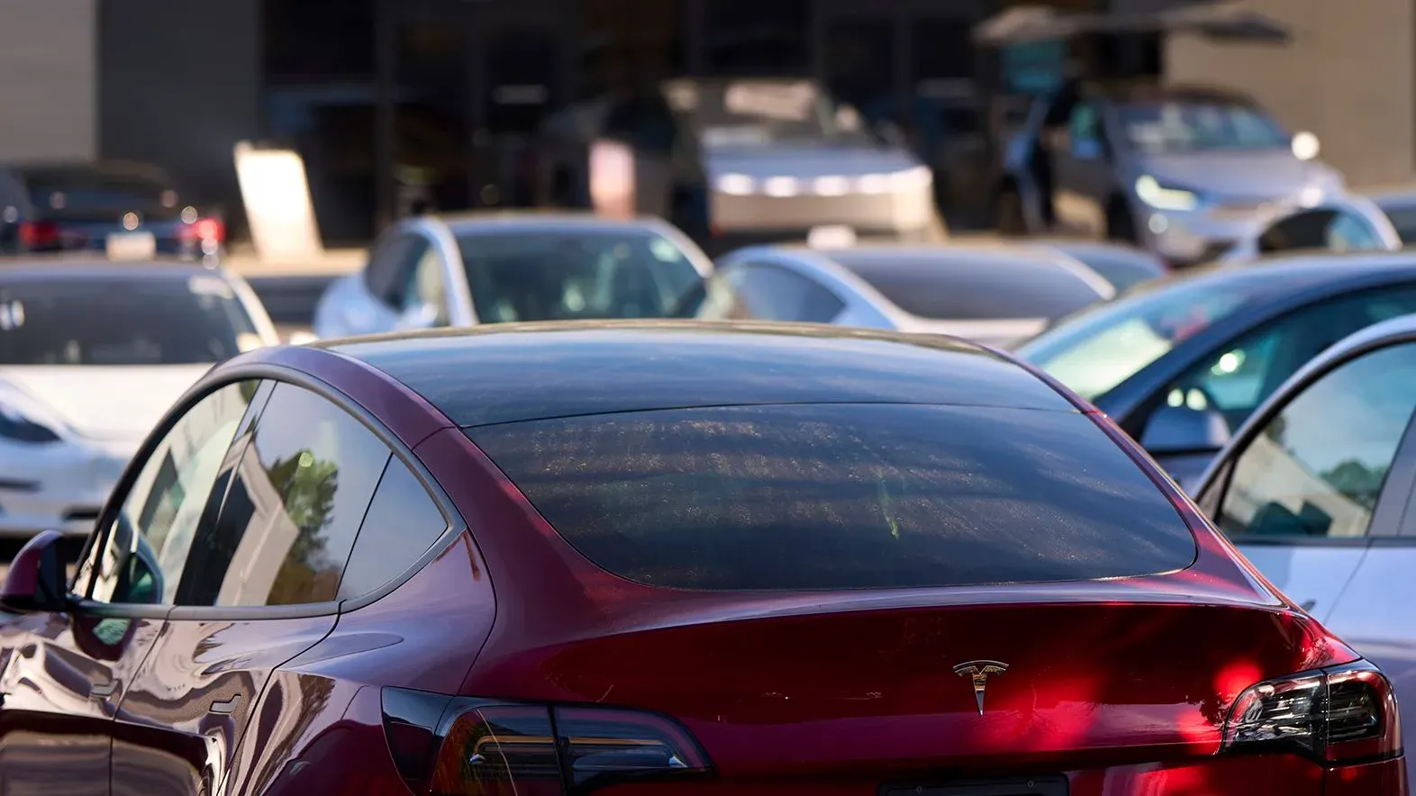 سيارة تسلا حمراء متوقفة في ساحة عرض، مع سيارات أخرى في الخلفية، تعكس تفوق تسلا في تصنيع السيارات الأمريكية.