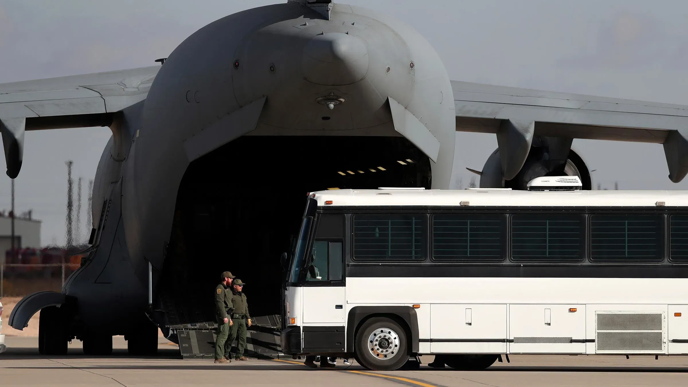 طائرة شحن عسكرية كبيرة في قاعدة فورت بليس، مع حافلة تنتظر لنقل المهاجرين المحتملين إلى منشآت الإيواء الجديدة.