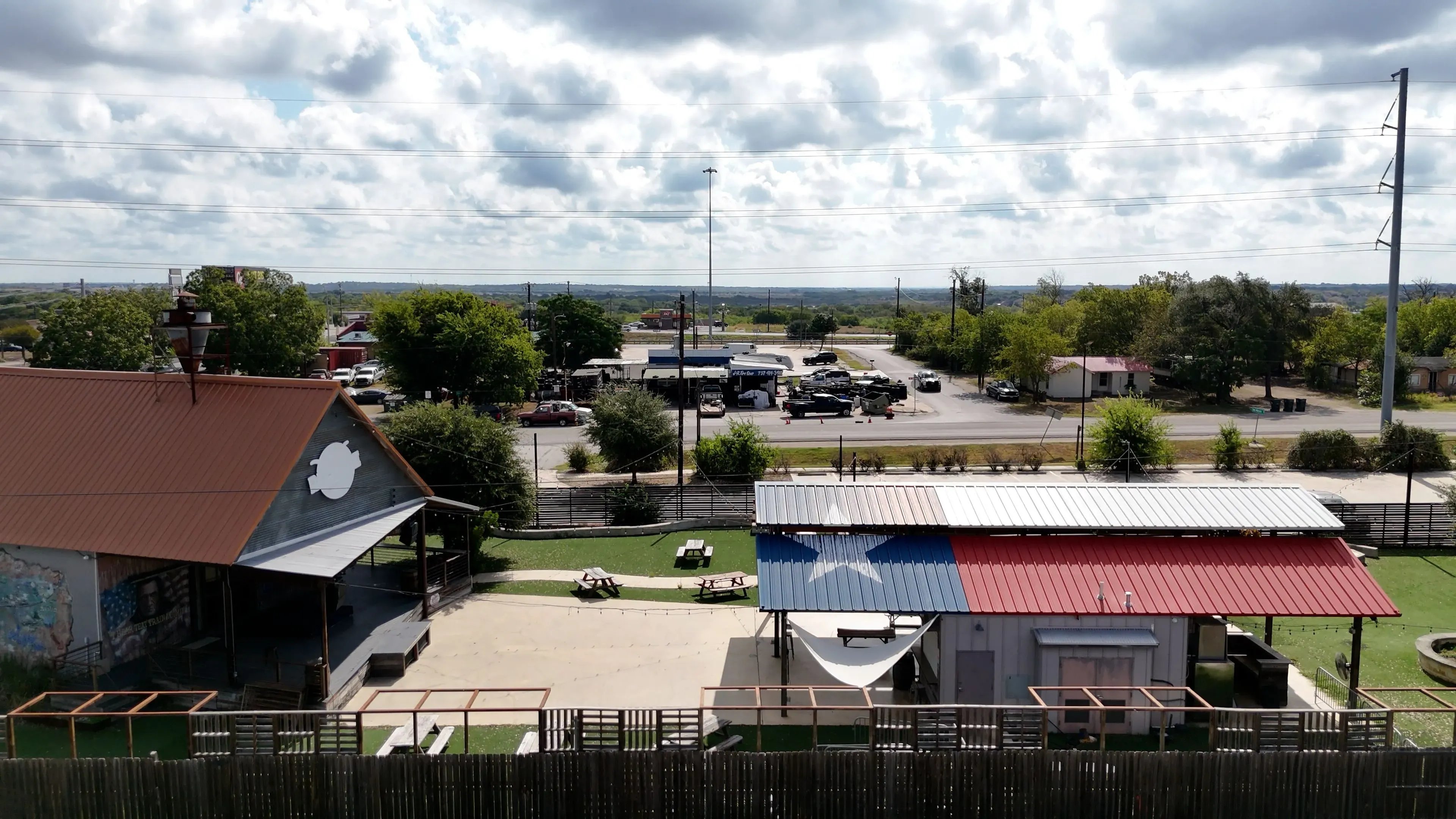 منظر لبلدة صغيرة في تكساس، يظهر مباني ذات أسطح ملونة وأعلام، مع خلفية طبيعية تتضمن أشجار وسحب في السماء.