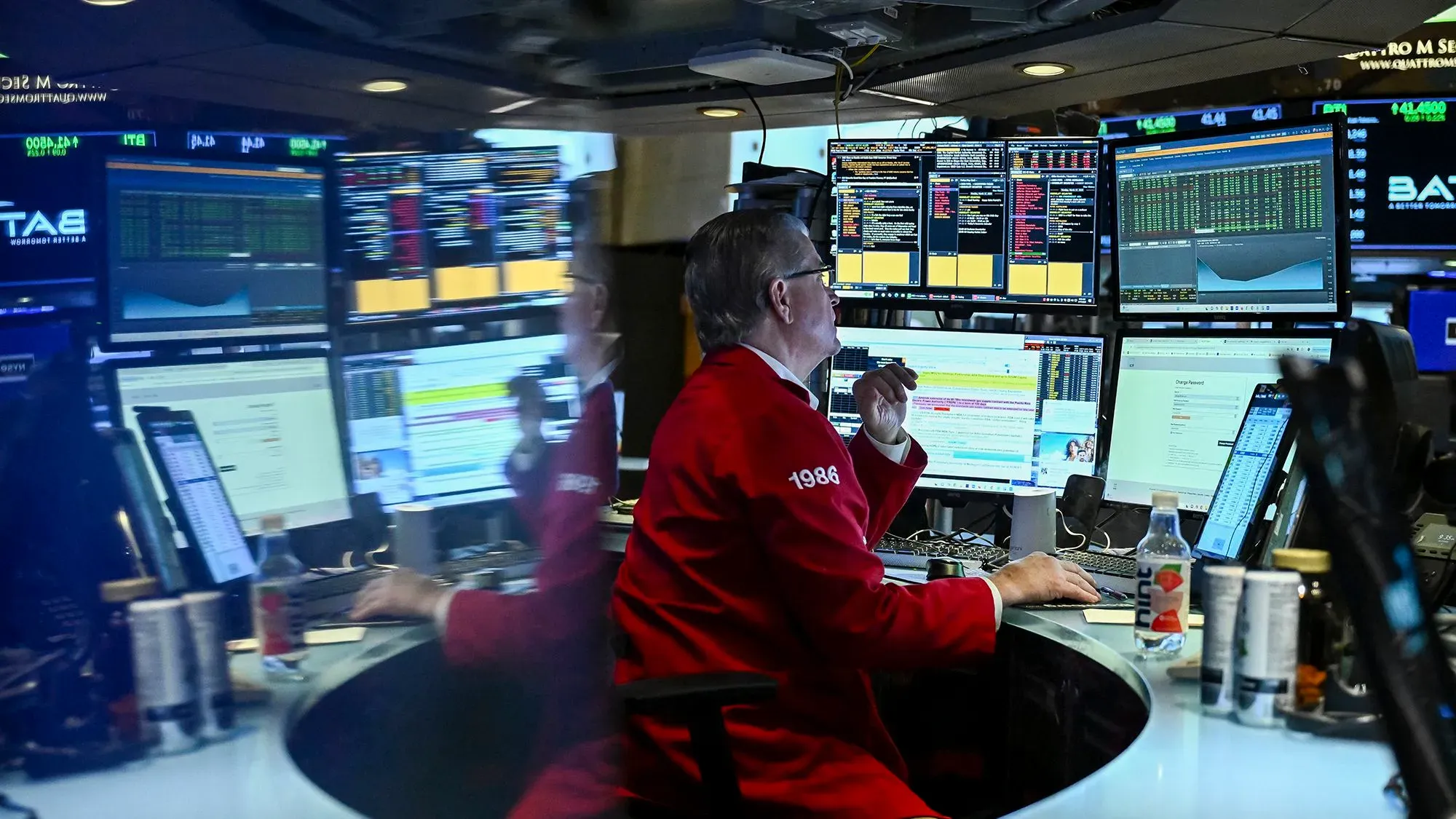 متداول في بورصة وول ستريت يرتدي سترة حمراء، محاط بشاشات تعرض بيانات السوق، يعبر عن القلق بشأن مستقبل الذكاء الاصطناعي.