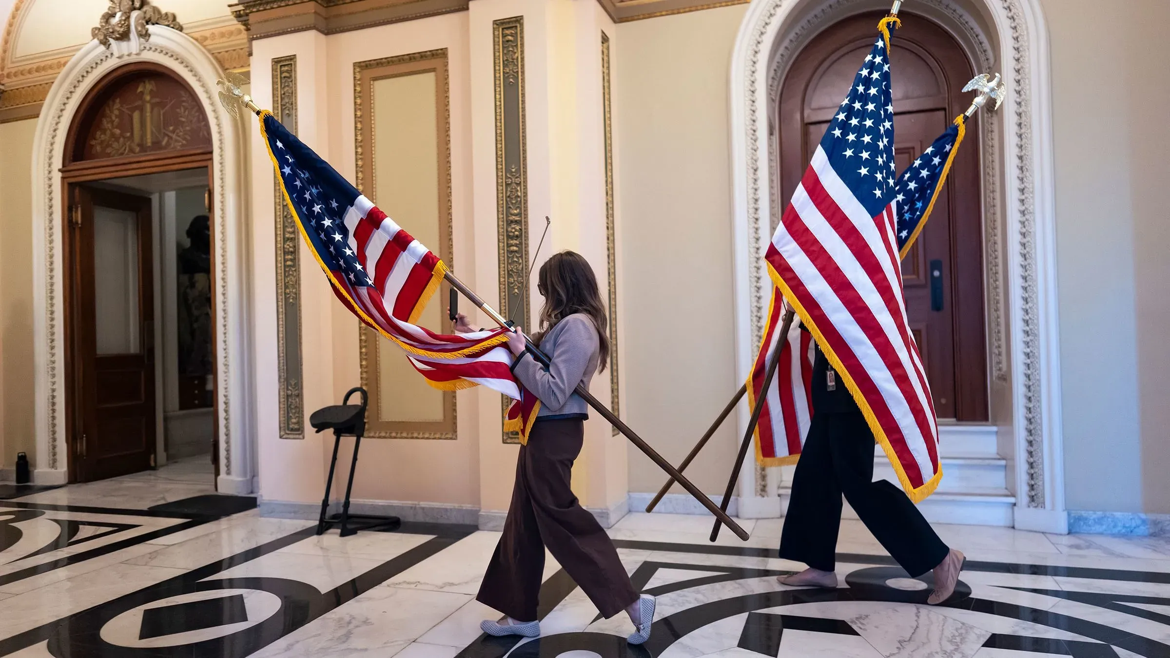 شخصان يحملان أعلام الولايات المتحدة داخل مبنى الكونغرس، مما يعكس أجواء النقاشات السياسية حول مشروع قانون الرعاية الطبية.