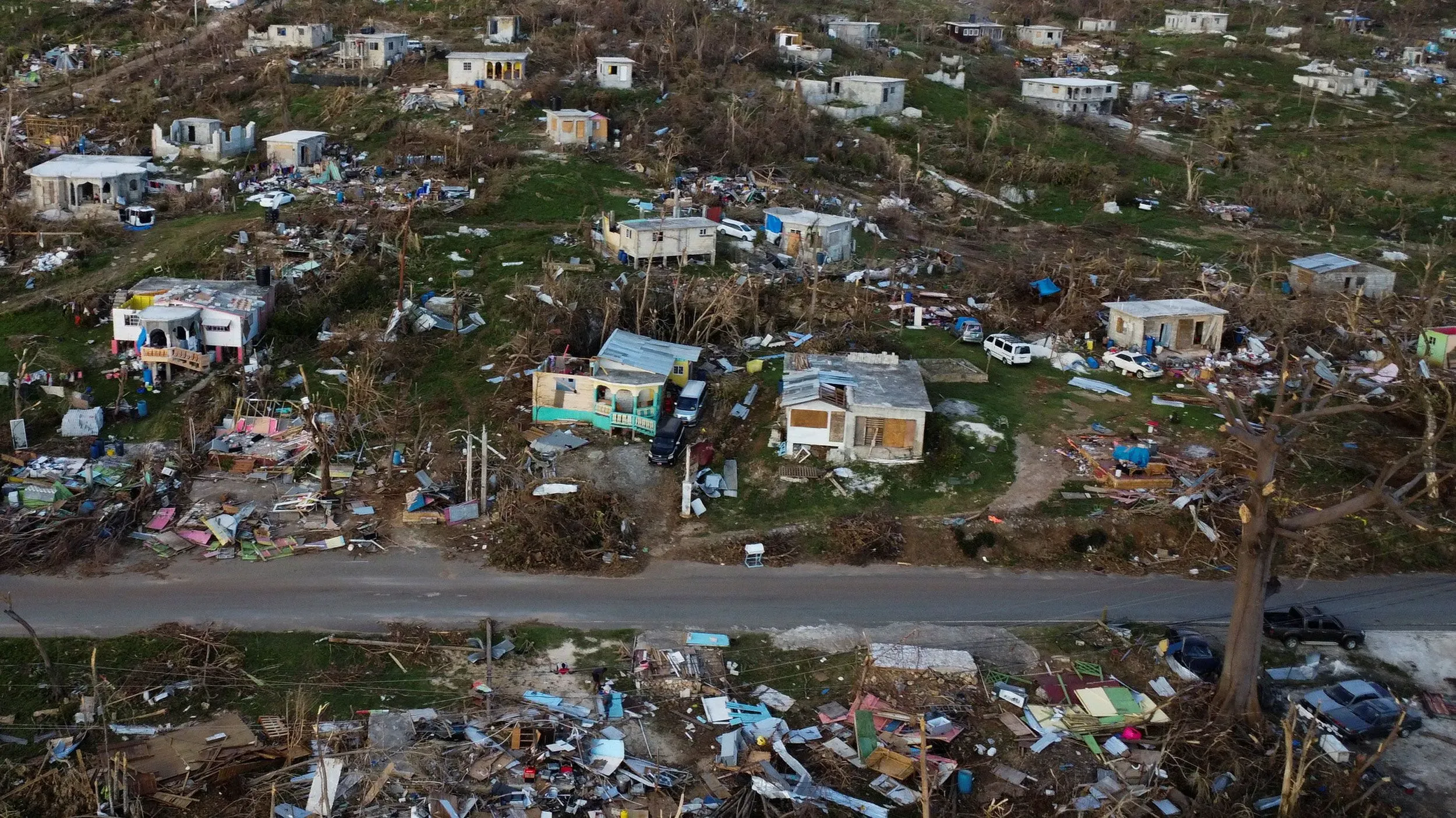 مشهد لقرية دمرتها الأعاصير، حيث تظهر المباني المهدمة والحطام في منطقة خضراء، مما يبرز تأثير العواصف القوية على المجتمعات.