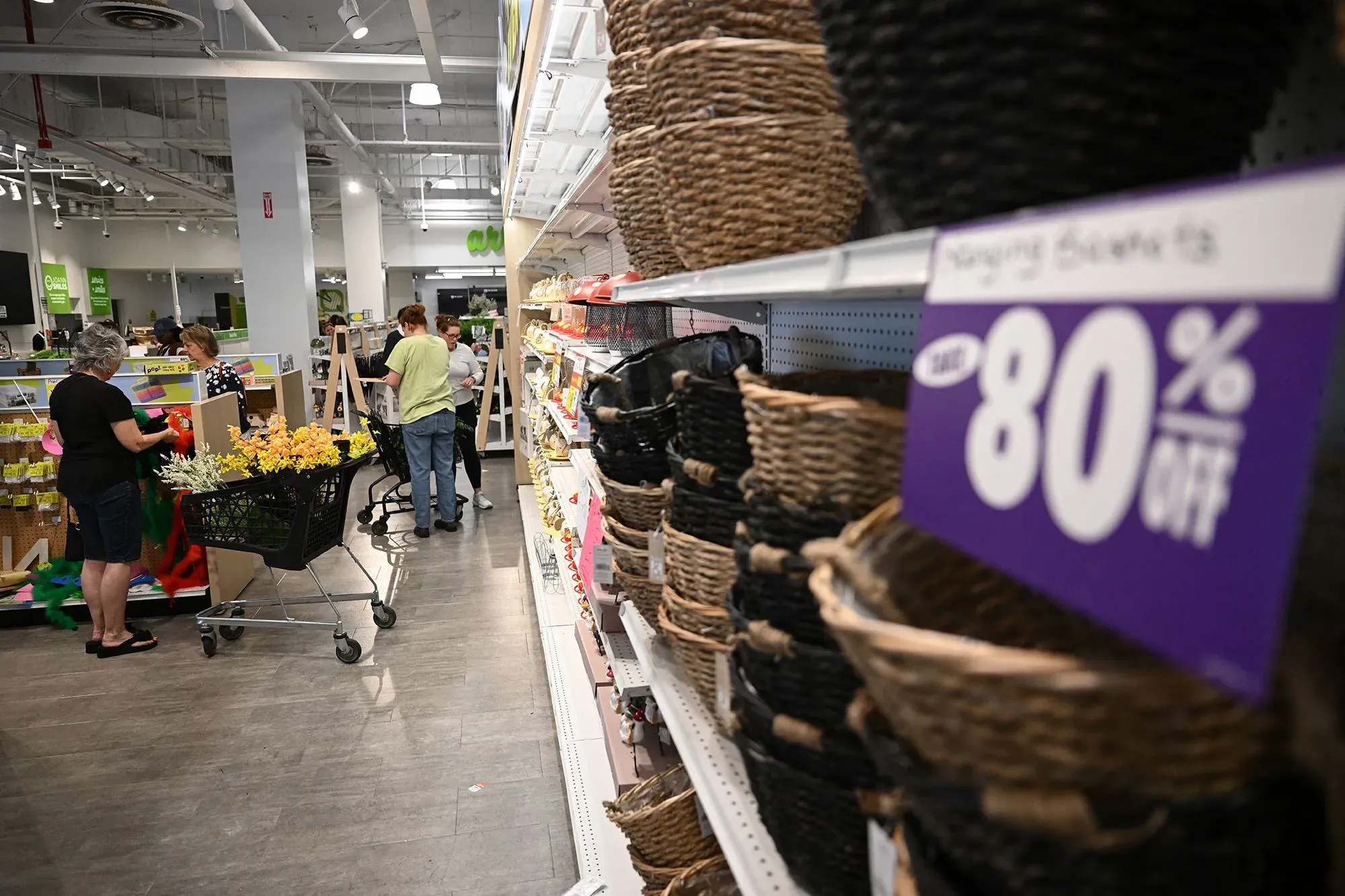 متسوقون في متجر يتجولون بين الأرفف، مع وجود لافتة تخفيضات تصل إلى 80% على السلع، مما يعكس تراجع تجارة التجزئة.