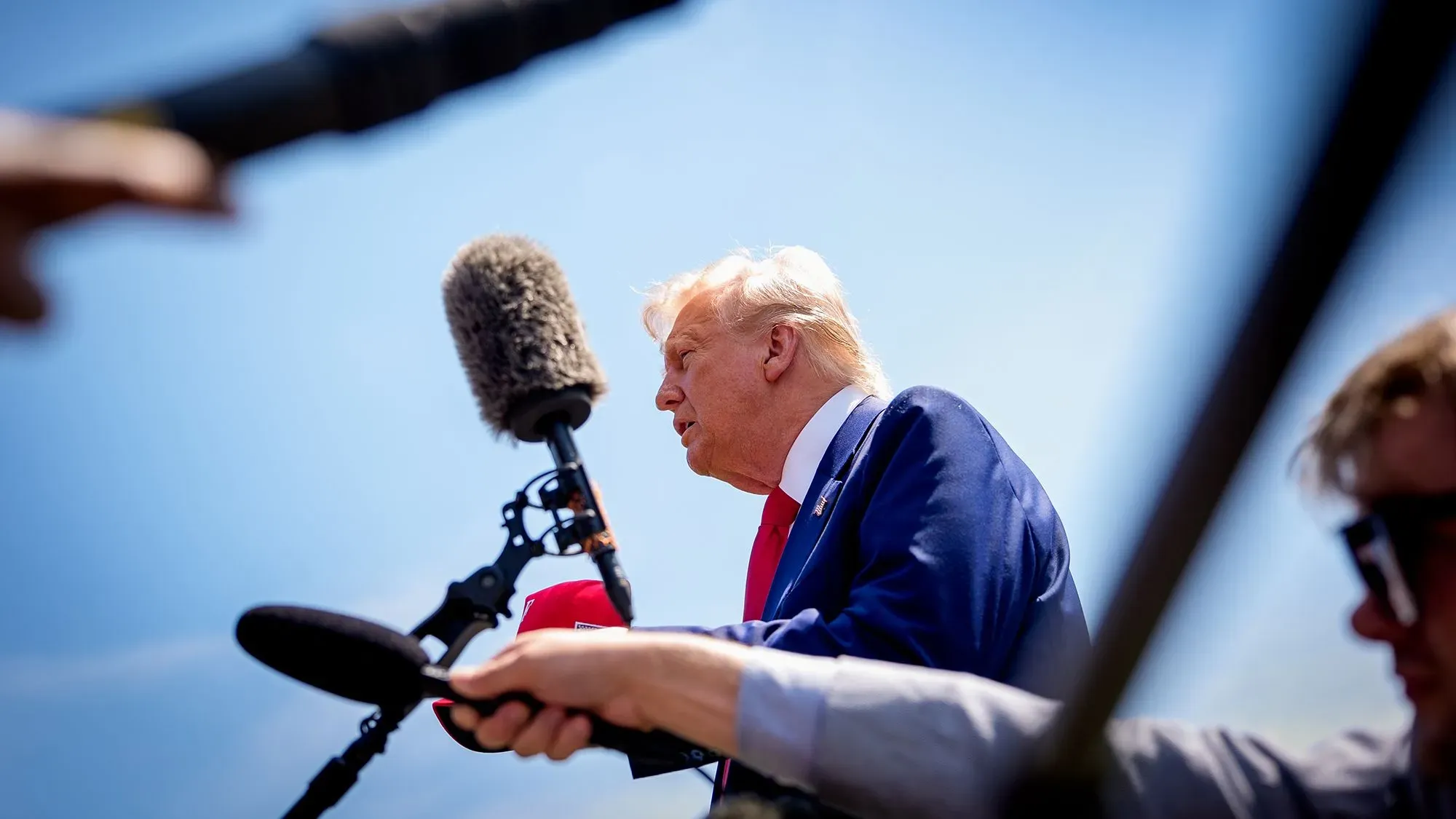 تصريح للرئيس ترامب خلال حدث عام، مع ميكروفونات ومصورين في الخلفية، يعكس التوجه نحو الفيديو بدلاً من النصوص الرسمية.