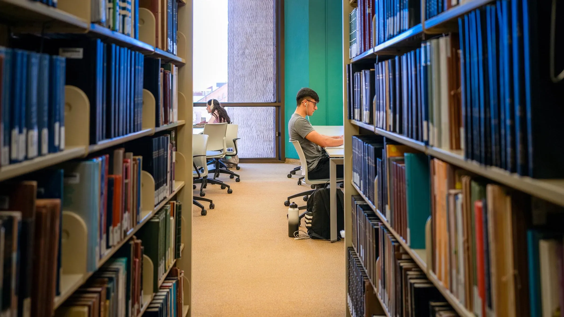 طلاب يجلسون في مكتبة، يركزون على دراستهم، وسط صفوف من الكتب، مما يعكس أهمية التعليم في ظل تغييرات قروض الطلاب.