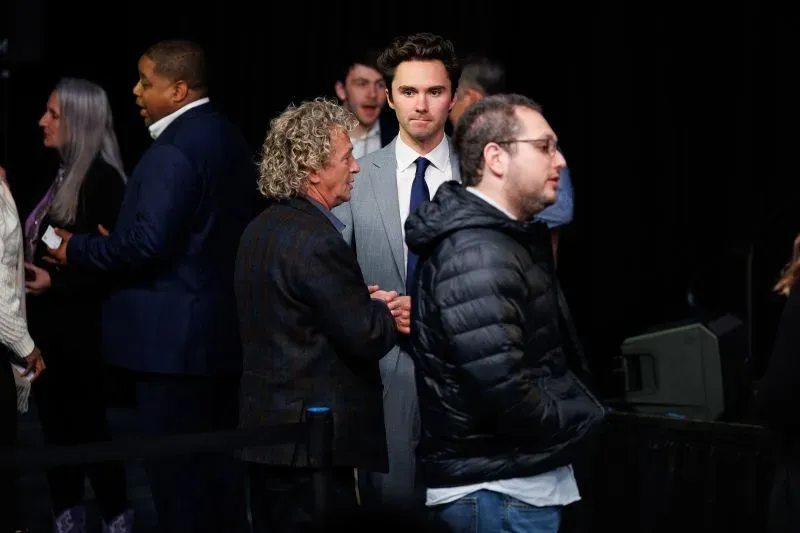 مجموعة من الأشخاص يتحدثون في حدث سياسي، مع التركيز على شاب يرتدي بدلة، مما يعكس التوترات داخل الحزب الديمقراطي.