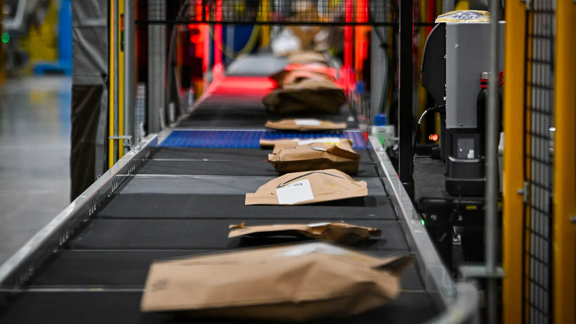 صناديق معبأة على سير متحرك في مركز توزيع أمازون، تعكس دعوة للمقاطعة ضد الشركة بسبب ممارساتها التجارية.