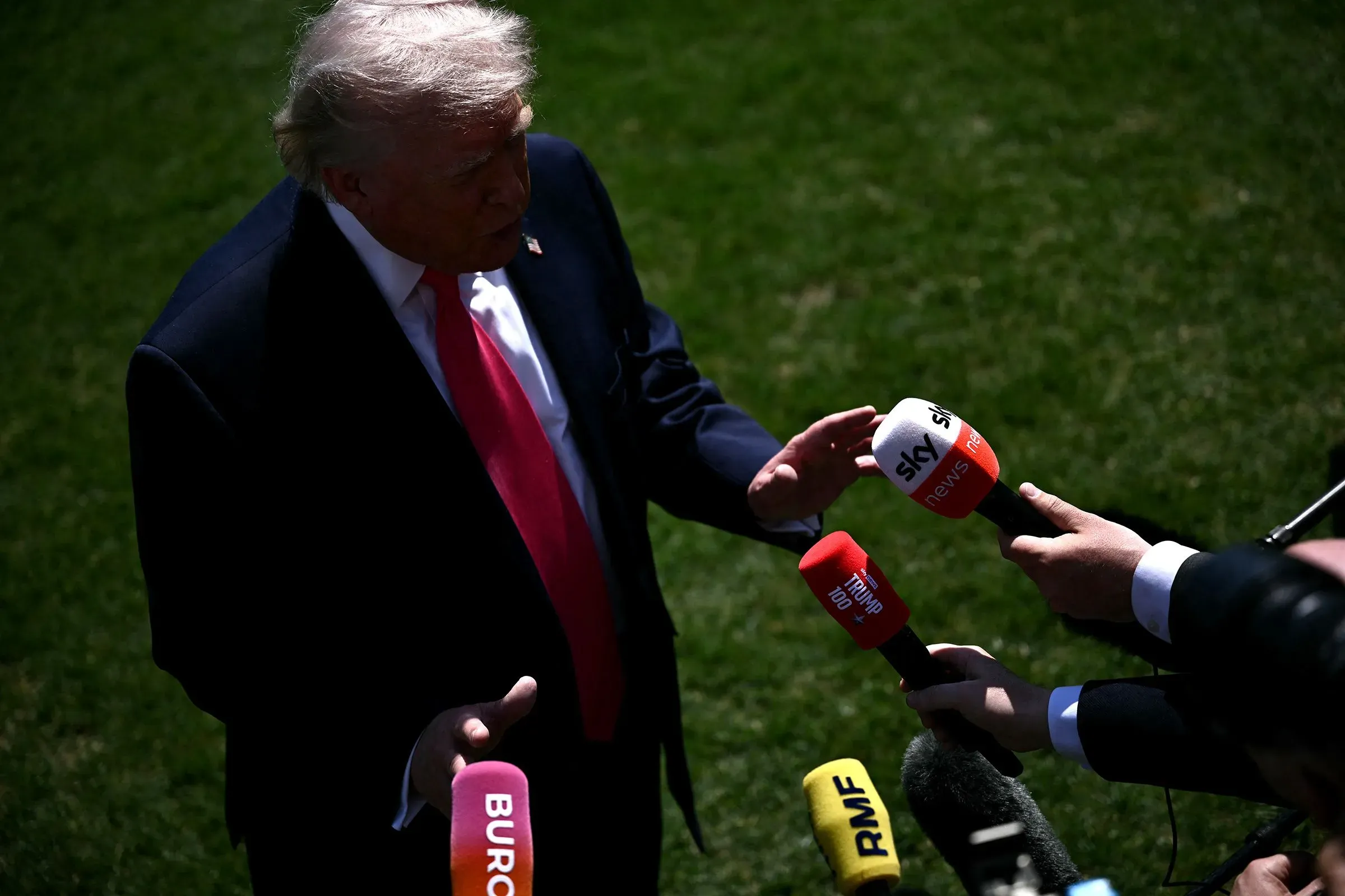 ترامب يتحدث إلى الصحفيين، محاطاً بميكروفونات متعددة، في سياق تهديدات تتعلق بإيران، مما يعكس ردود الفعل السياسية حول تصريحاته.
