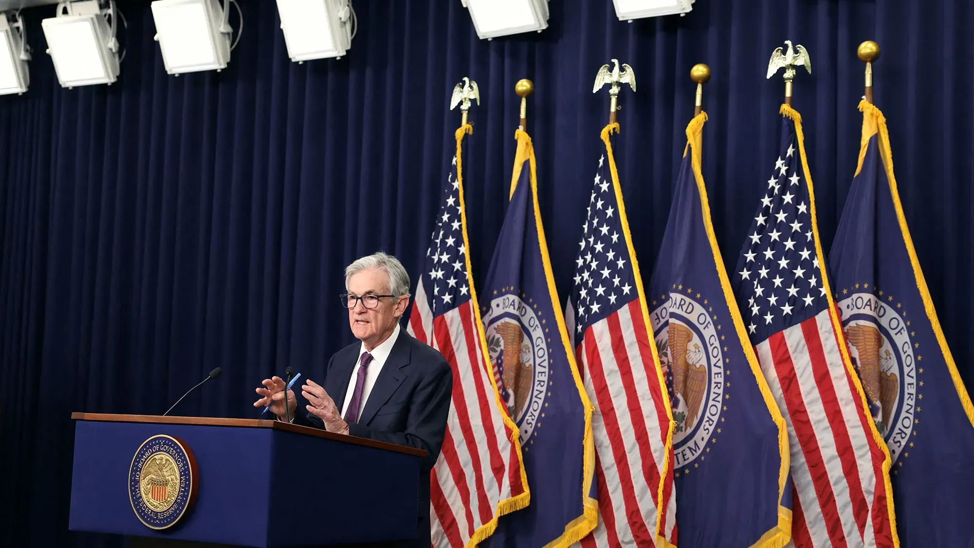 جيروم باول، رئيس الاحتياطي الفيدرالي، يتحدث خلال مؤتمر صحفي مع وجود أعلام الولايات المتحدة خلفه، مع التركيز على السياسة النقدية.