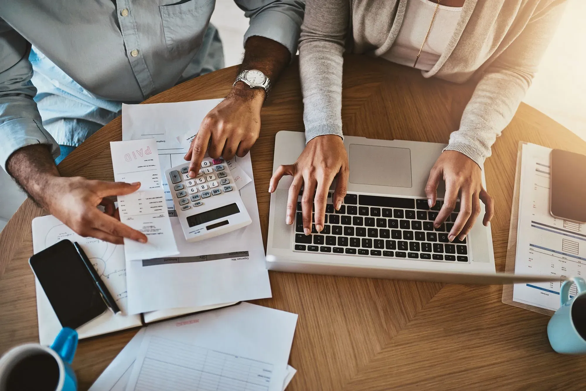 شخصان يعملان على حسابات مالية، مع أوراق ومستندات حول الطاولة، تعكس أهمية إدارة المدخرات والديون في ظل تغييرات أسعار الفائدة.