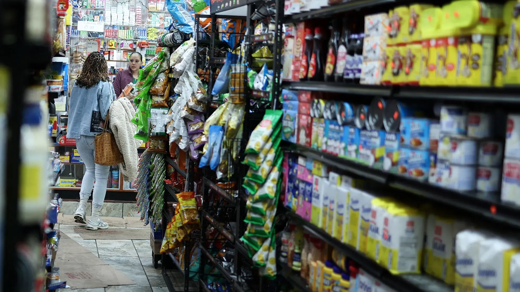 امرأتان تتسوقان في ممر متجر مليء بالمنتجات الغذائية، مع التركيز على تراجع إنفاق المستهلكين في يناير.