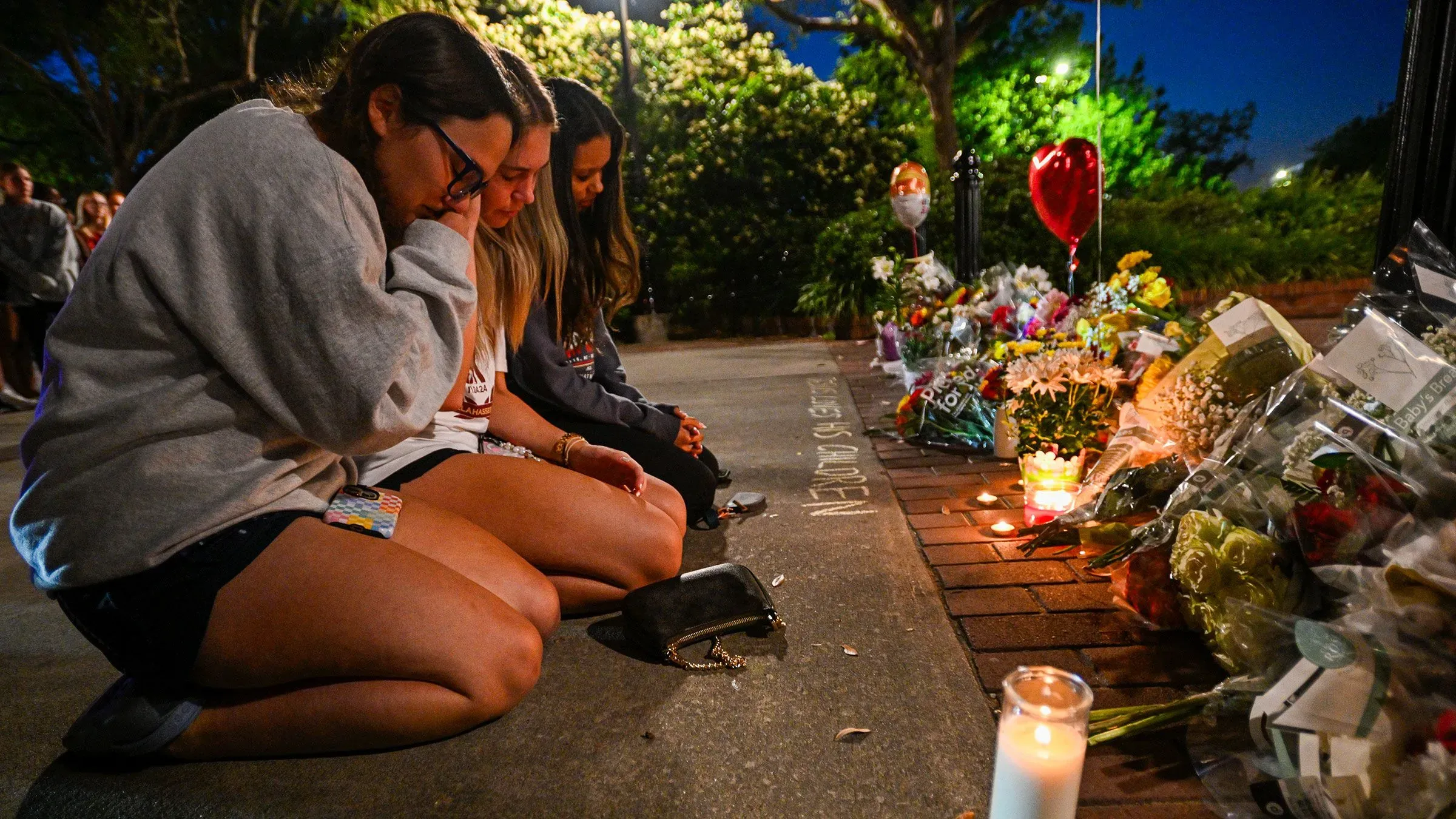 طالبات يجلسن على الأرض في حرم جامعة ولاية فلوريدا، يعبرن عن حزنهن أمام أكاليل الزهور والشموع المضيئة تخليداً لذكرى الضحايا.