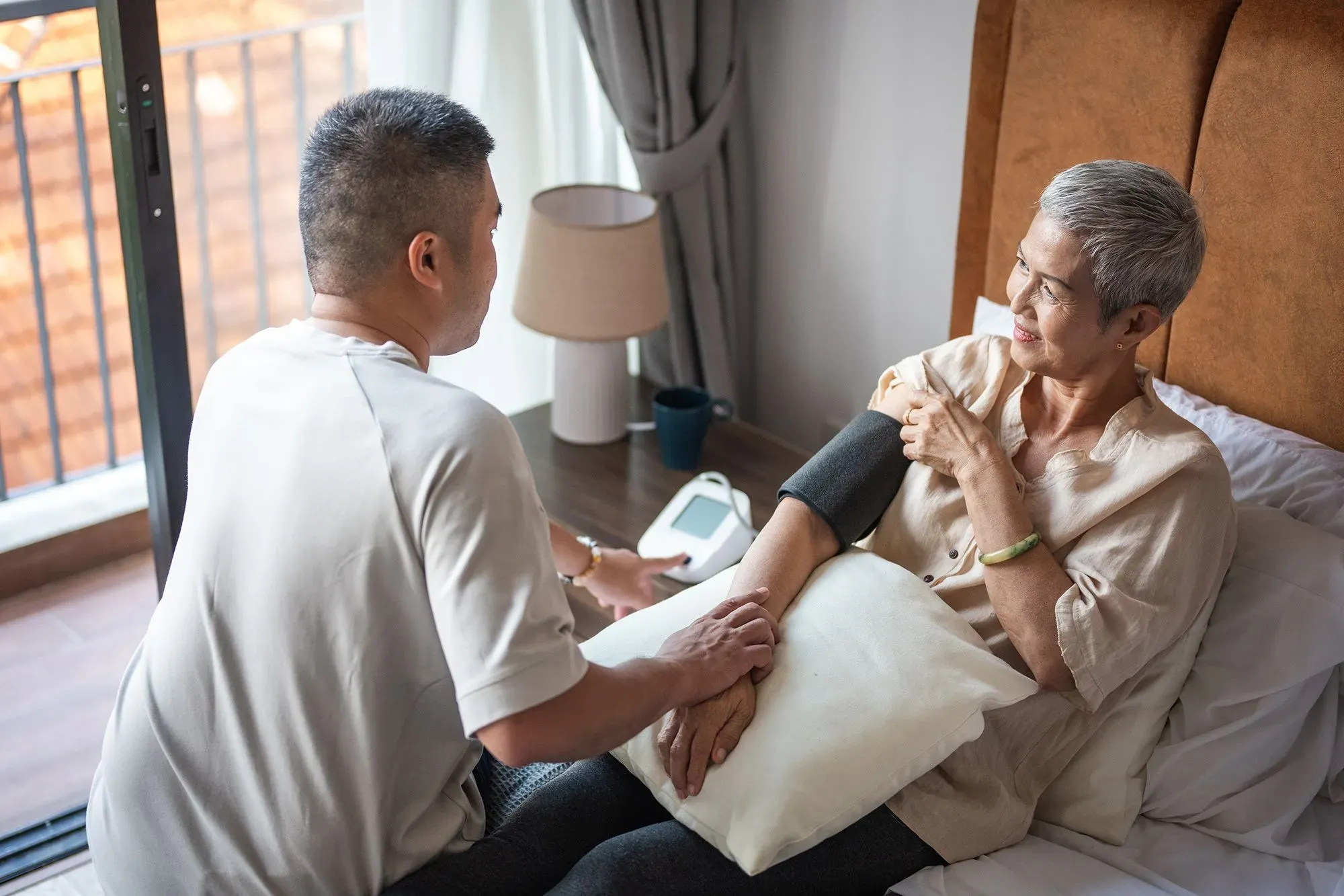 رجل يساعد امرأة مسنّة في قياس ضغط الدم داخل غرفة معيشة، مما يعكس دور مقدمي الرعاية في دعم الأهل المتقدمين في السن.