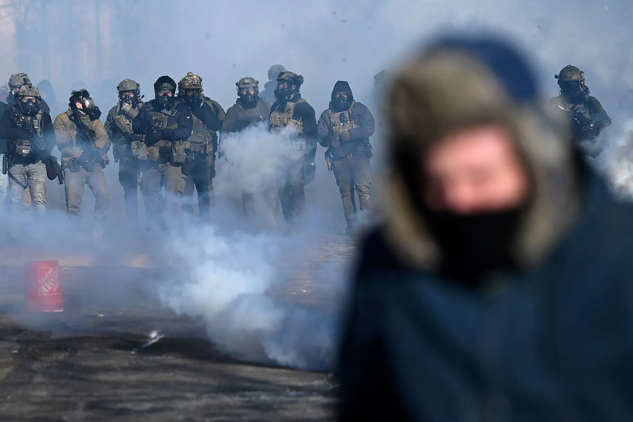 مواجهة بين قوات الأمن والمتظاهرين في منطقة ملبدة بالغيوم بالدخان، مع وجود أفراد يرتدون ملابس عسكرية وأقنعة واقية.