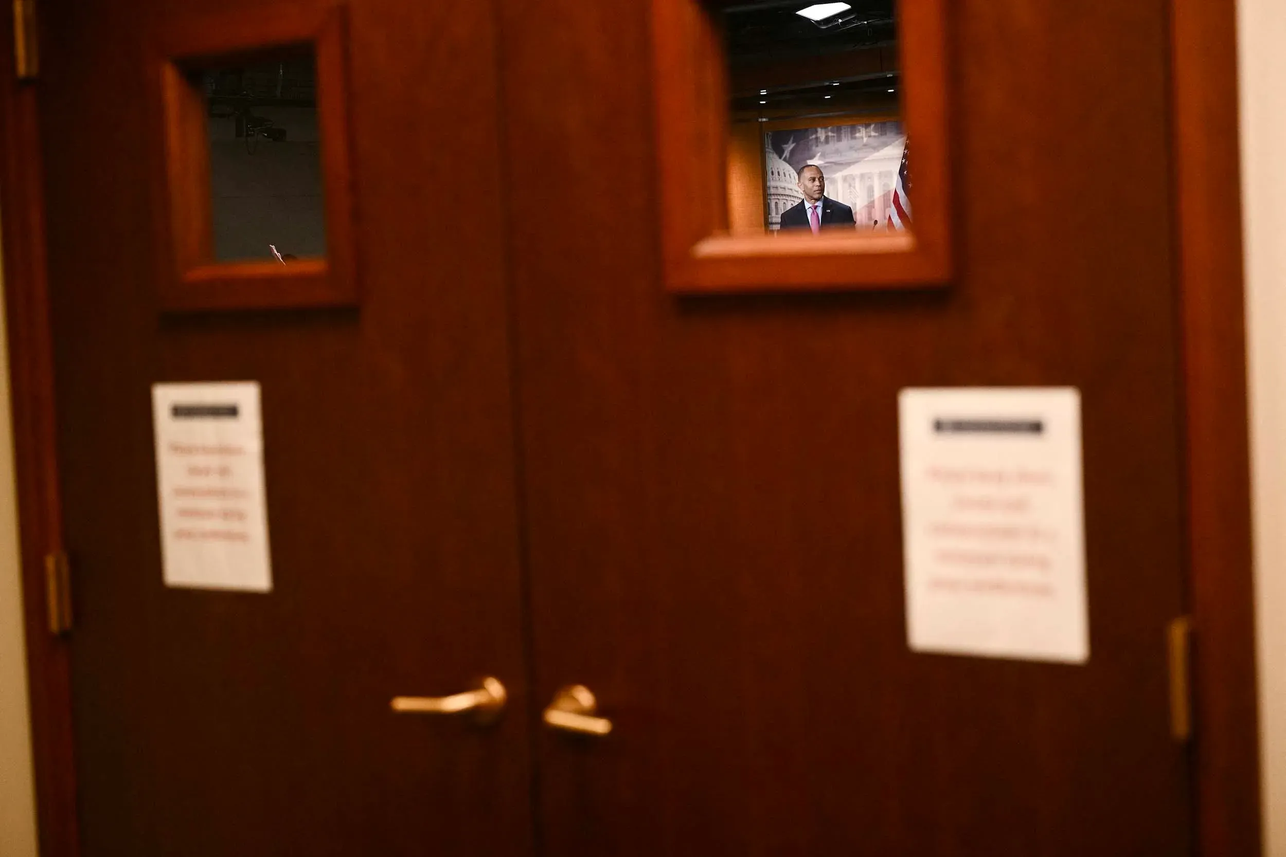 صورة تظهر شخصًا يقف خلف باب مغلق مع نافذة زجاجية، في سياق دراما الإغلاق الحكومي والضغط السياسي المتزايد في واشنطن.