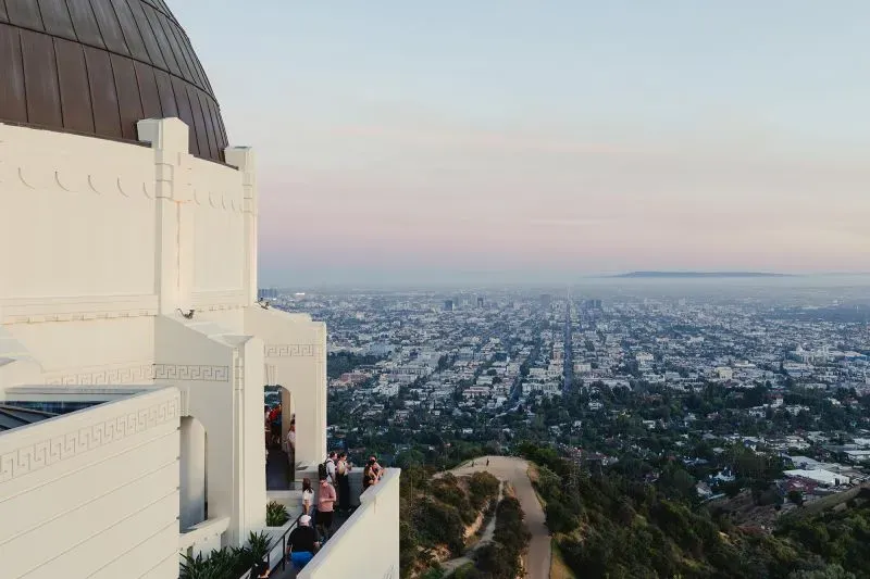 منظر بانورامي لمرصد غريفيث في لوس أنجلوس، مع وجود زوار يستمتعون بالمناظر الخلابة للمدينة في وقت الغروب.