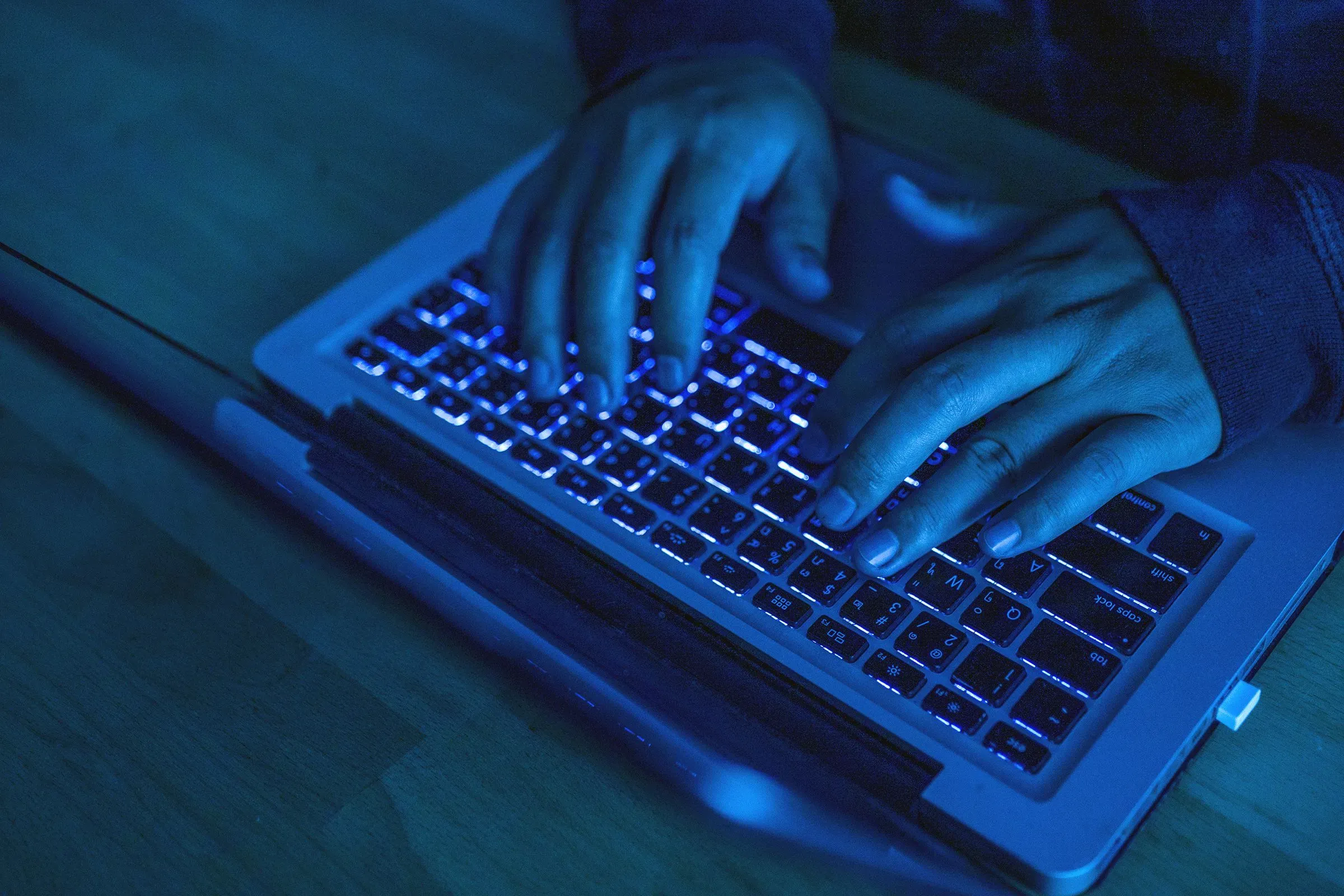 أيدٍ تعمل على لوحة مفاتيح كمبيوتر محمول في بيئة مظلمة، تعكس التهديدات الإلكترونية المتزايدة في عالم الجرائم السيبرانية.