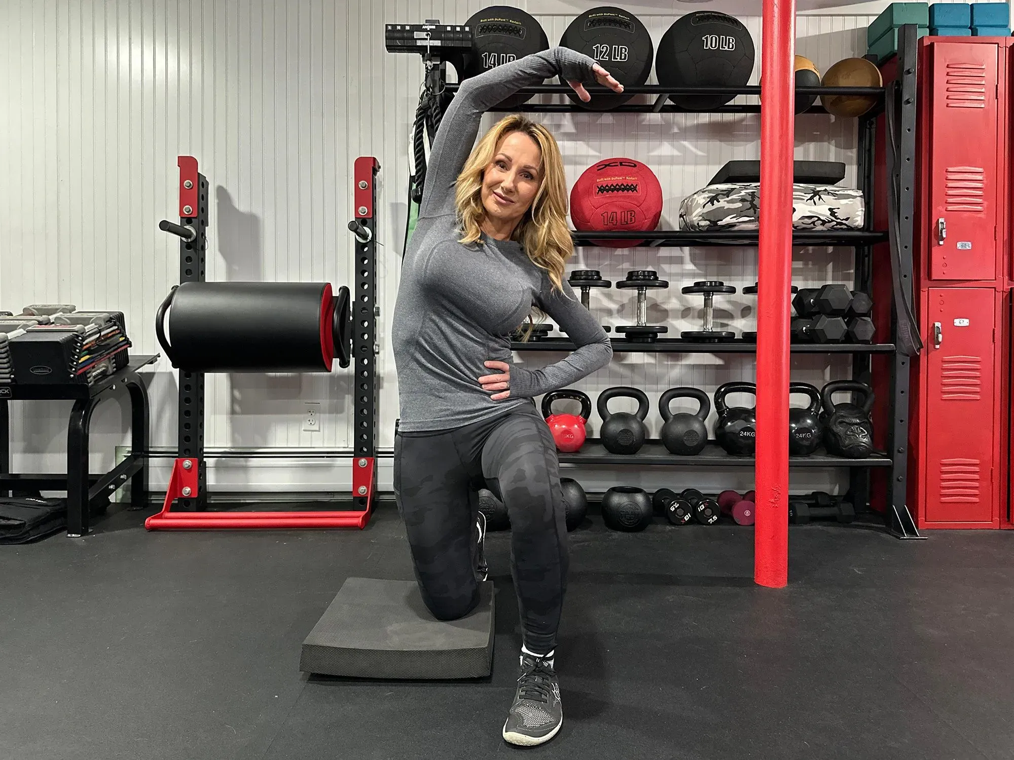 امرأة تؤدي تمريناً لتقوية عضلات الورك، في صالة رياضية تحتوي على معدات رياضية متنوعة، مما يعكس أهمية التمارين لتحسين صحة أوتار المأبض.