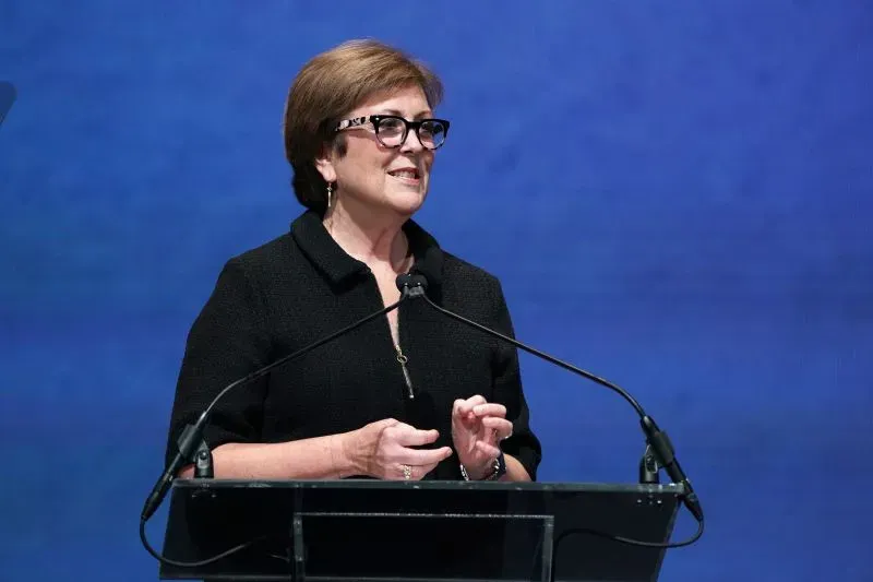 امرأة تتحدث على المنصة في مركز كينيدي، مع خلفية زرقاء، تعكس أهمية الفنون ودورها في التعبير الثقافي.