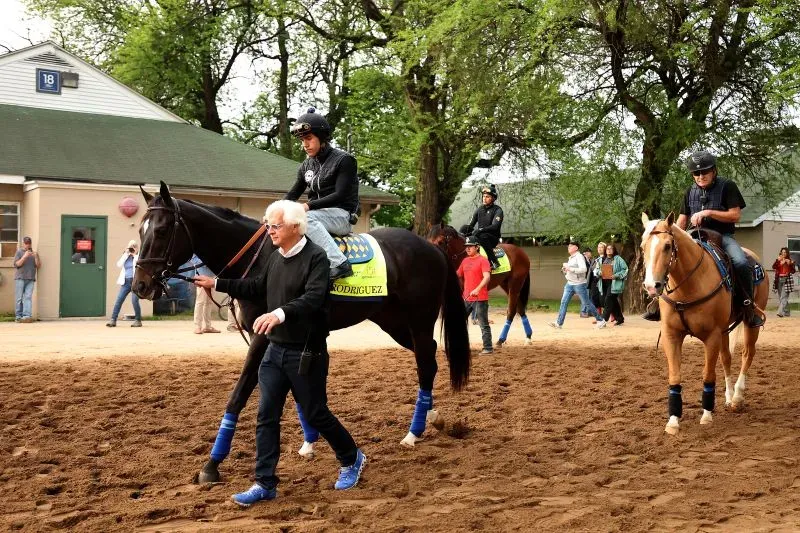 بوب بافرت، مدرب الخيول الشهير، يقود حصاناً خلال تدريب في مضمار سباق، وسط مجموعة من المتسابقين والمشاهدين.