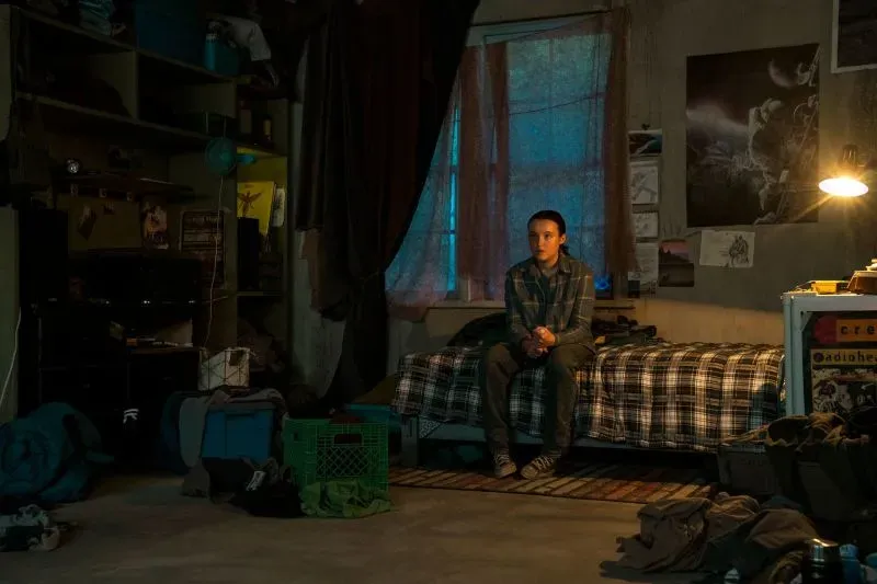 إيلي تجلس بمفردها في غرفتها المظلمة، محاطة بأغراض فوضوية، تعكس شعورها بالوحدة والتوتر في أحداث مسلسل "The Last of Us".