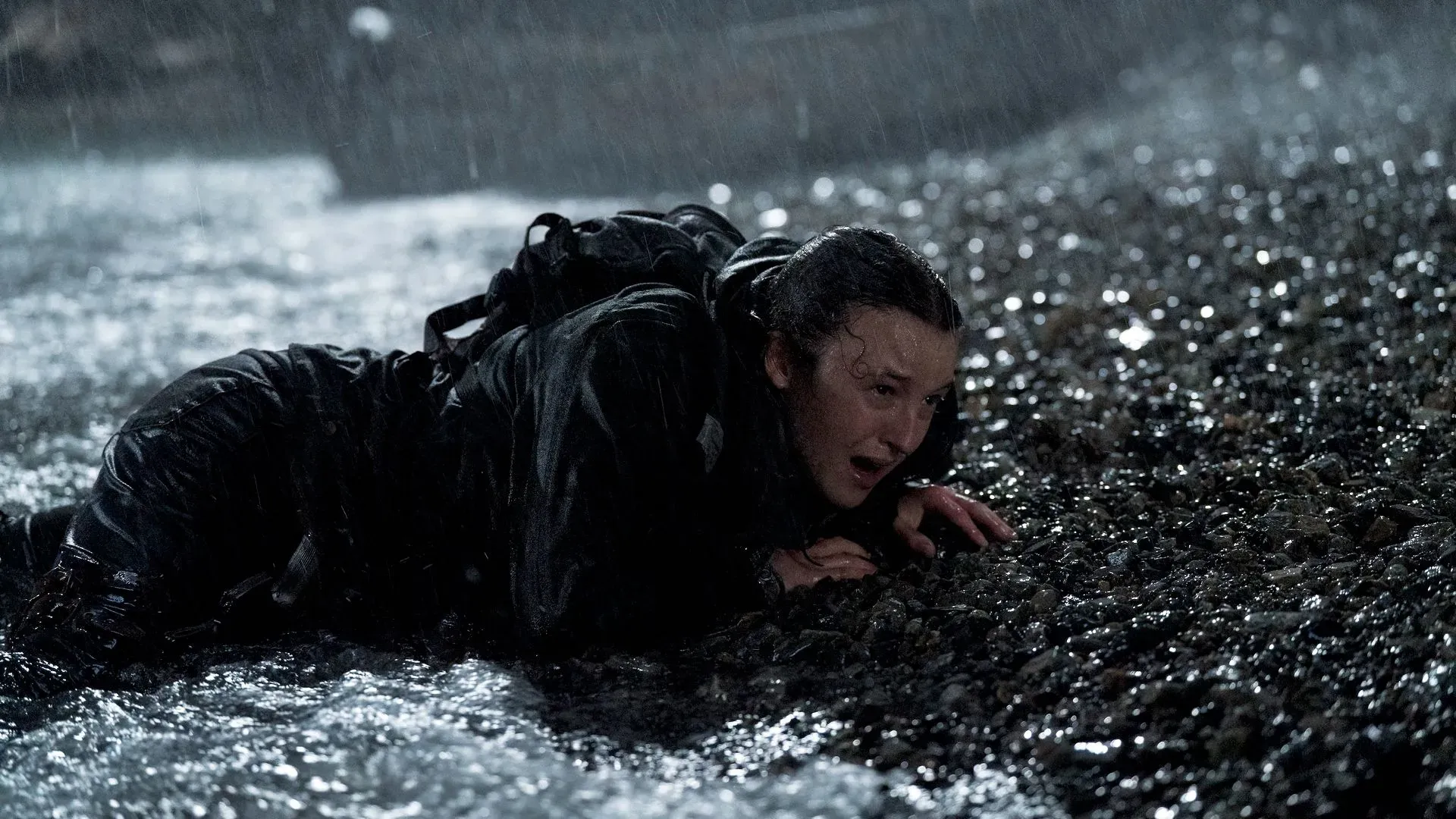 إيلي تتدحرج على الأرض تحت المطر، تعبيرها يعكس الألم والقلق في مشهد مثير من مسلسل "The Last of Us".