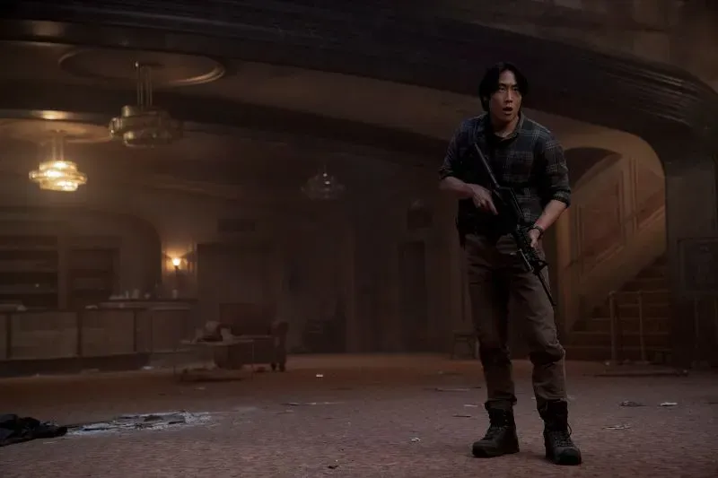 جيسي، الشخصية الرئيسية في "The Last of Us"، يقف في مسرح مظلم ممسكًا بسلاحه، محاطًا بأجواء مشحونة بالتوتر.