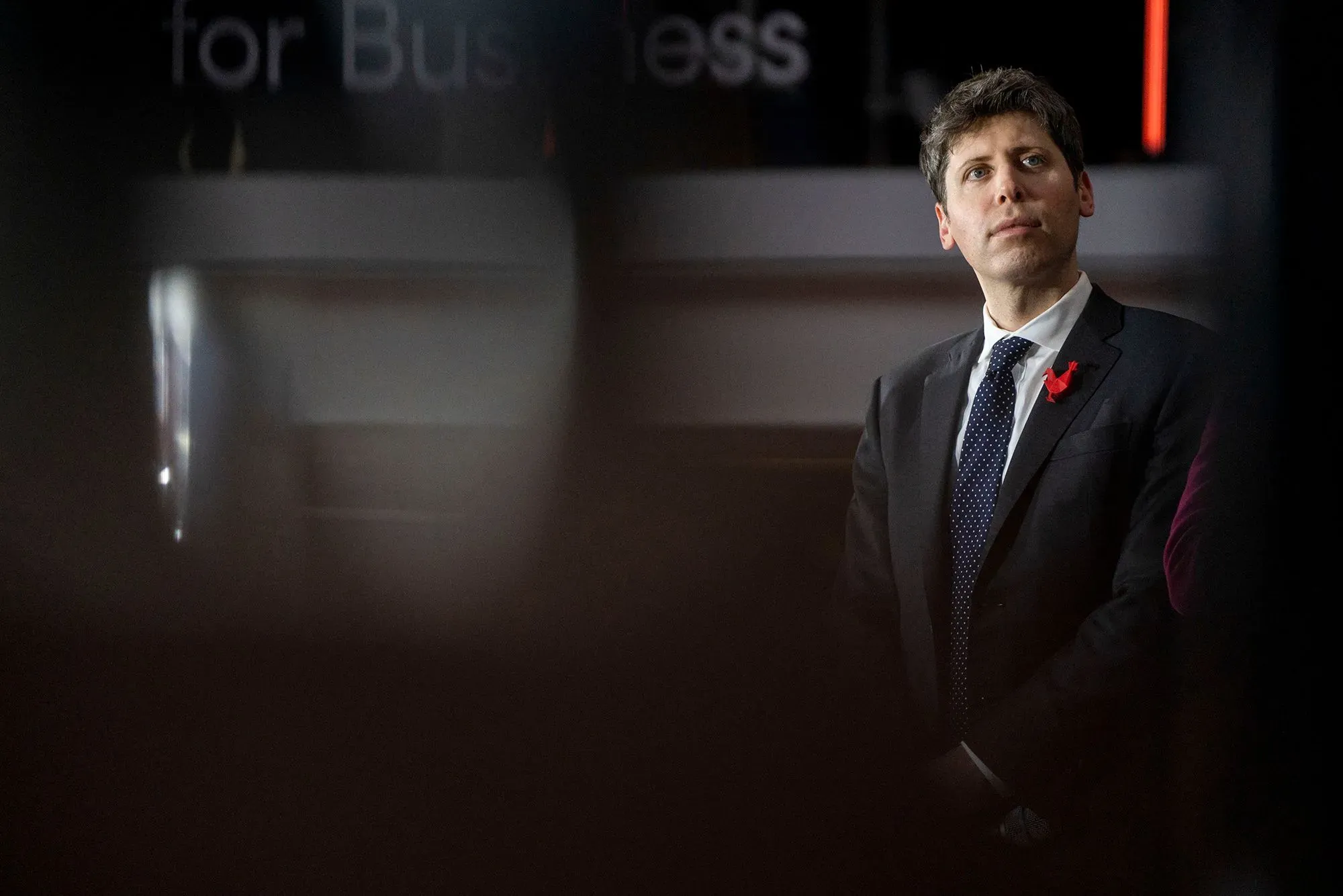 صورة لسام ألتمان، الرئيس التنفيذي لشركة OpenAI، وهو يرتدي بدلة رسمية ويبدو في حالة تفكير عميق خلال حدث متعلق بالذكاء الاصطناعي.