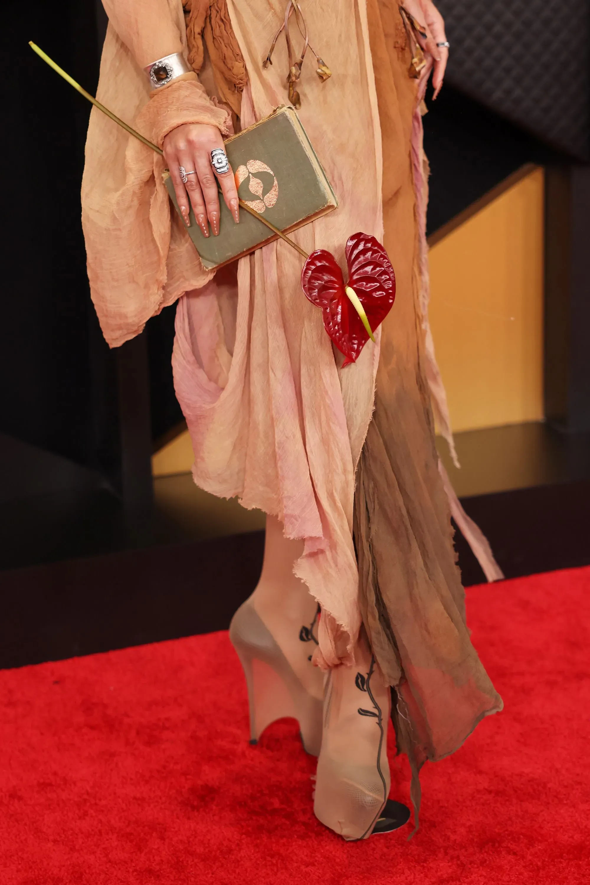 إطلالة فريدة على السجادة الحمراء، حيث ترتدي الشخصية فستاناً مميزاً مع حذاء عالٍ وحقيبة مزينة بزهور، تعكس أسلوباً جريئاً ومبتكراً.