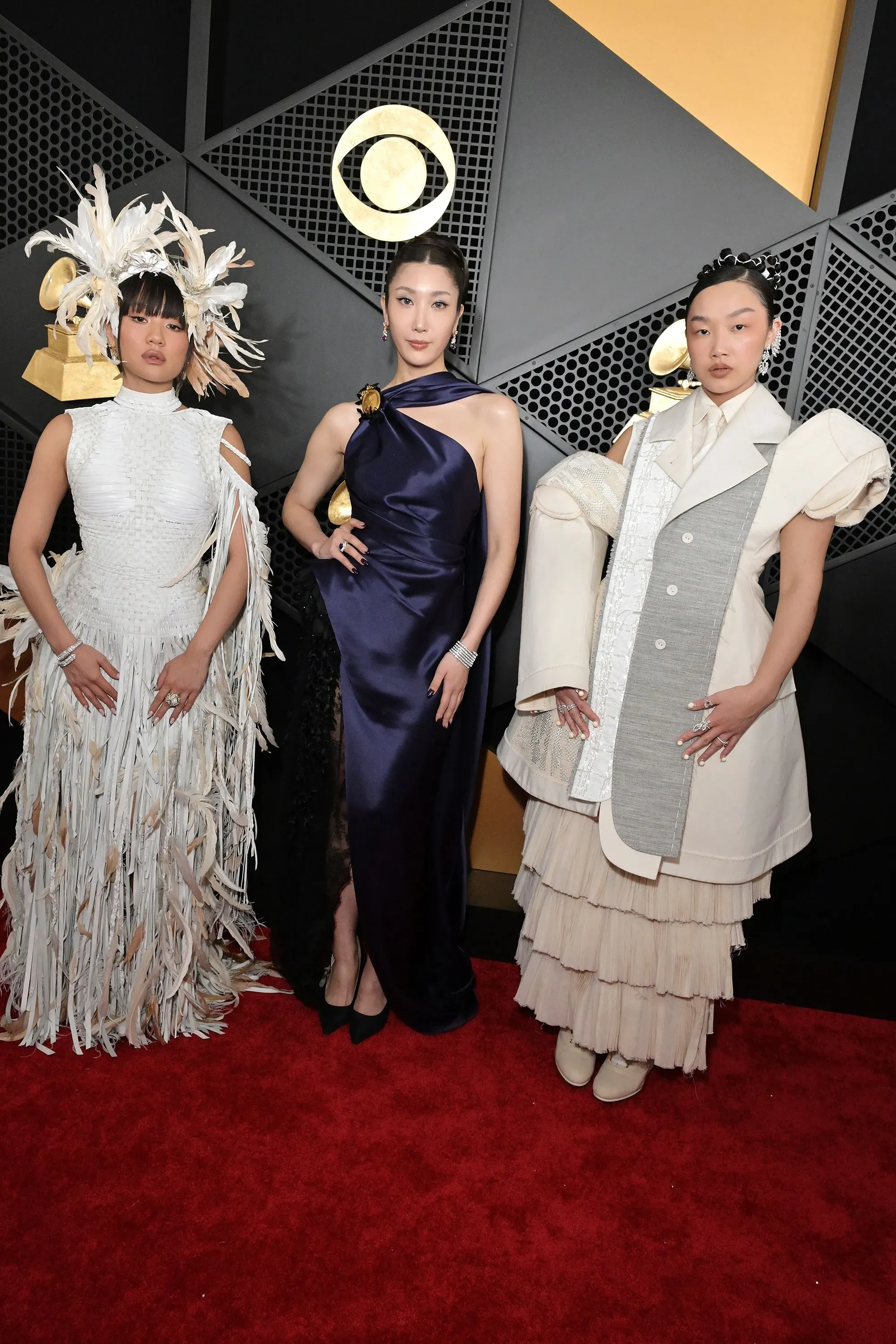 ثلاث نساء يرتدين أزياء مميزة على السجادة الحمراء لحفل توزيع جوائز غرامي، مع تفاصيل فنية تعكس أسلوب الموضة المعاصر.