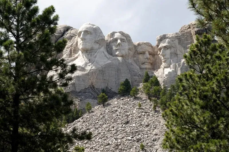 منظر لجبل راشمور في داكوتا الجنوبية، حيث تمثال لوجوه أربعة رؤساء أمريكيين، محاط بأشجار خضراء وصخور.