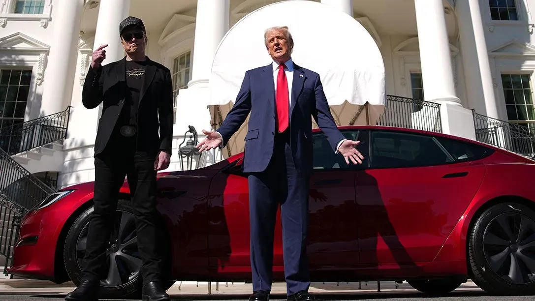 ترامب يقف أمام سيارة تسلا حمراء، مع إيلون ماسك بجانبه، في حديقة البيت الأبيض، مع إبراز التوتر بينهما.