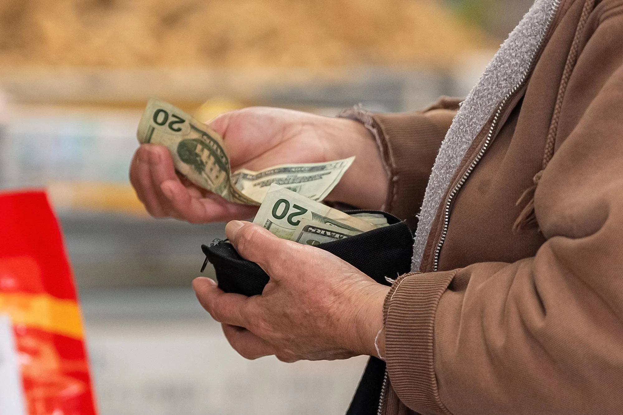 يد شخص مسن يعد أوراق نقدية من فئة 20 دولارًا، يعكس تأثير الدين الأمريكي الضخم على الأفراد والقدرة الشرائية.