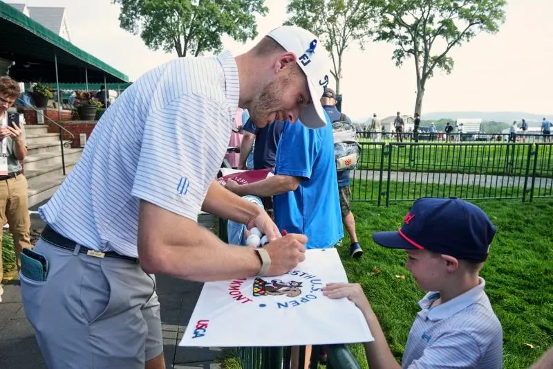 مات فوغت، لاعب جولف وطبيب أسنان، يوقع على لافتة لصبي صغير خلال بطولة أمريكا المفتوحة، مع تعابير الفرح والإلهام.