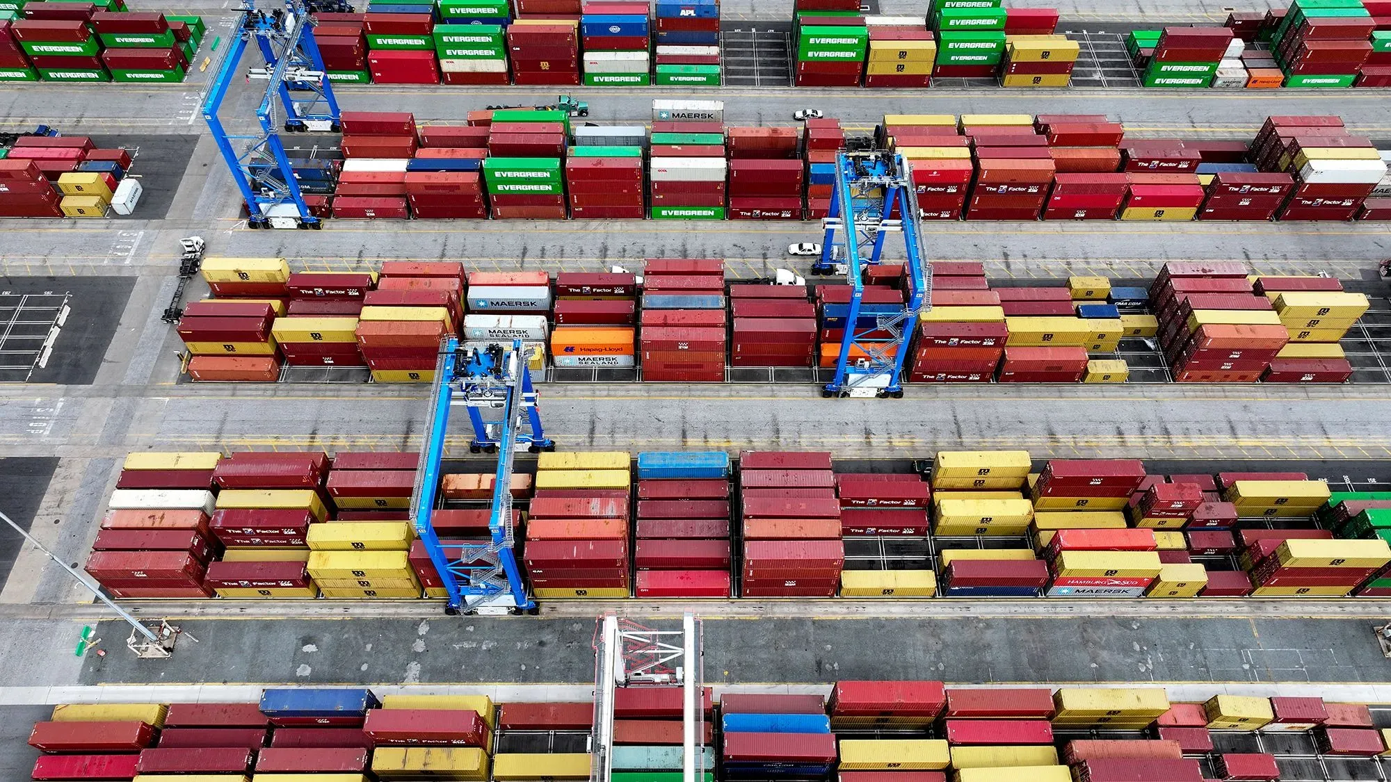 صورة جوية لميناء يحتوي على حاويات متعددة الألوان، تعكس تأثير الرسوم الجمركية الجديدة على التجارة العالمية.