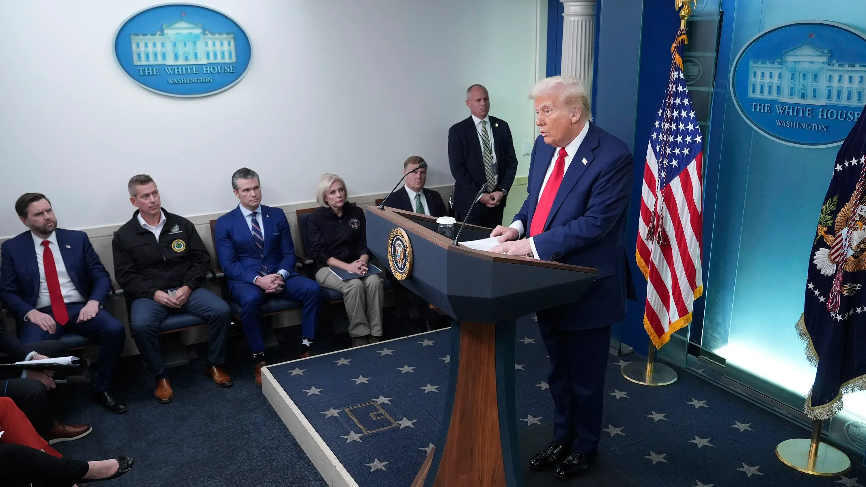 ترامب يتحدث أمام الصحافة في البيت الأبيض، محاطاً بمساعدين وخلفه شعار البيت الأبيض، بينما يتناول قضايا الحكومة والطيران.