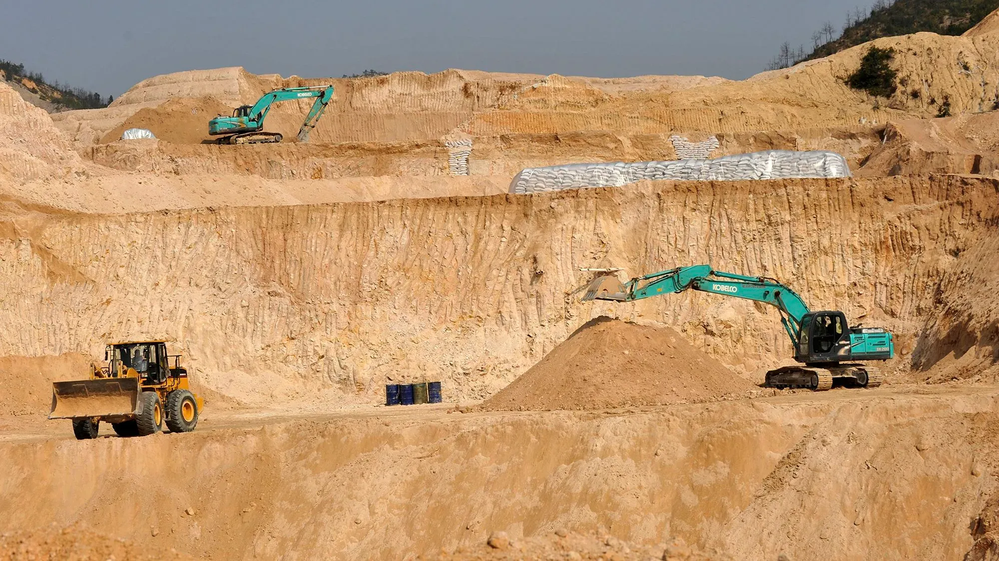 موقع تعدين يحتوي على جرافات وآلات ثقيلة تعمل على استخراج المعادن الأرضية النادرة، وسط تربة مكشوفة.