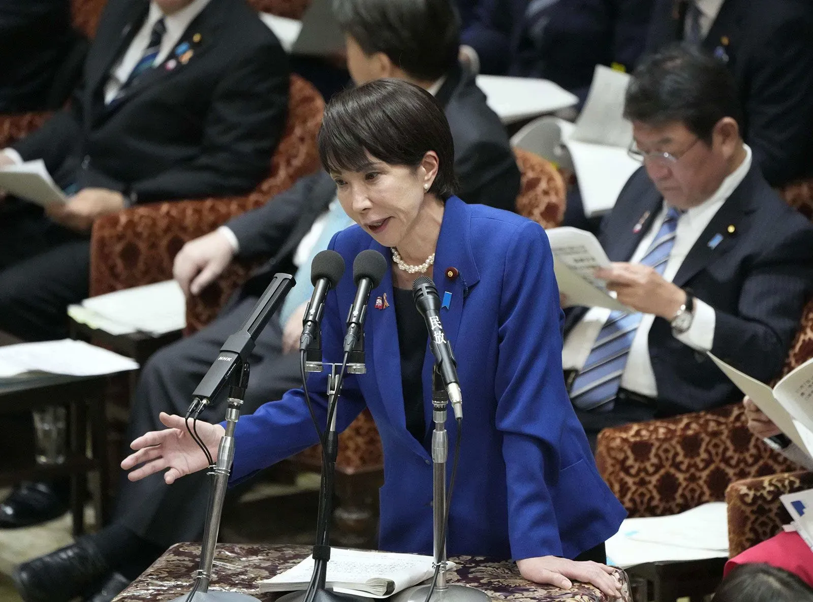 سناء تاكايتشي، وزيرة اليابان، تتحدث في البرلمان حول التوترات مع الصين بشأن تايوان، بينما يظهر الحضور في الخلفية.