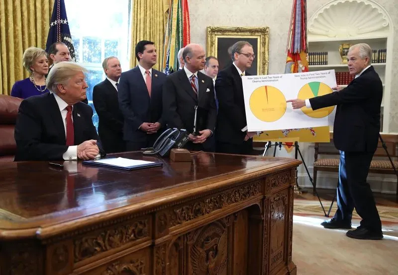 اجتماع في المكتب البيضاوي حيث يتحدث مستشار ترامب الاقتصادي بيتر نافارو، بينما يجلس ترامب مع فريقه، مع عرض بياني يوضح البيانات الاقتصادية.