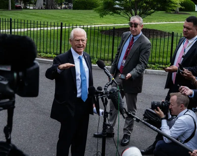 بيتر نافارو يتحدث أمام الصحفيين في البيت الأبيض، محاطًا بكاميرات ومراسلين، مع خلفية خضراء من الأشجار والأسوار.