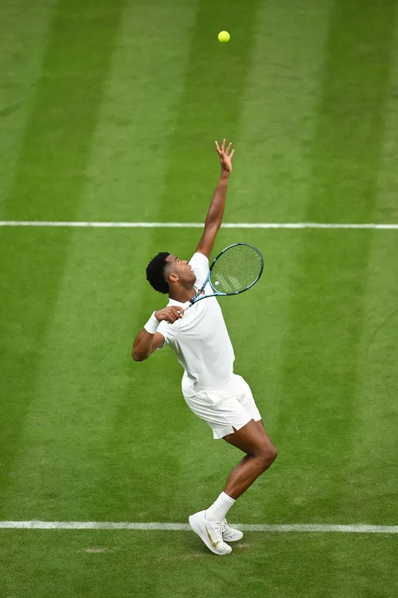 لاعب تنس يستعد لإرسال الكرة في بطولة ويمبلدون، يظهر تقنية الإرسال القوية على الملعب الأخضر.