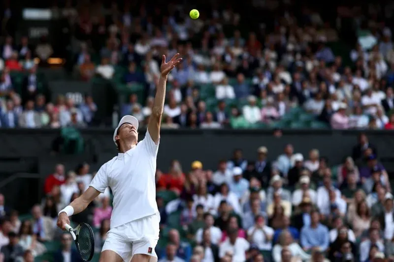 لاعب تنس يستعد لإرسال الكرة في بطولة ويمبلدون، مع جمهور كبير في الخلفية، مما يعكس أهمية السرعة والدقة في اللعبة.