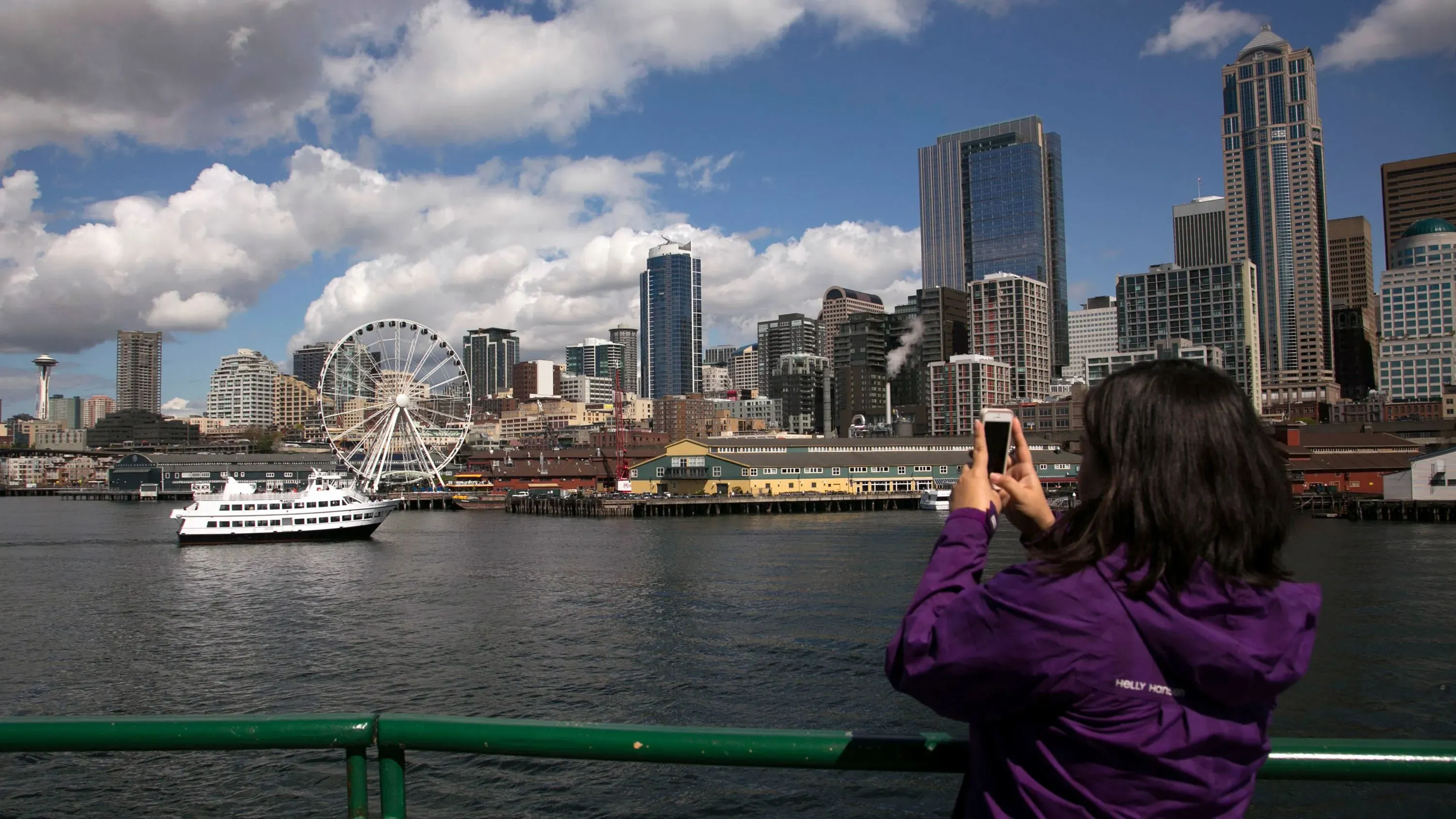 امرأة تلتقط صورة لمدينة سياتل، تظهر العجلة الدوارة والمباني الشاهقة، مما يعكس تأثير انخفاض السياحة الكندية.