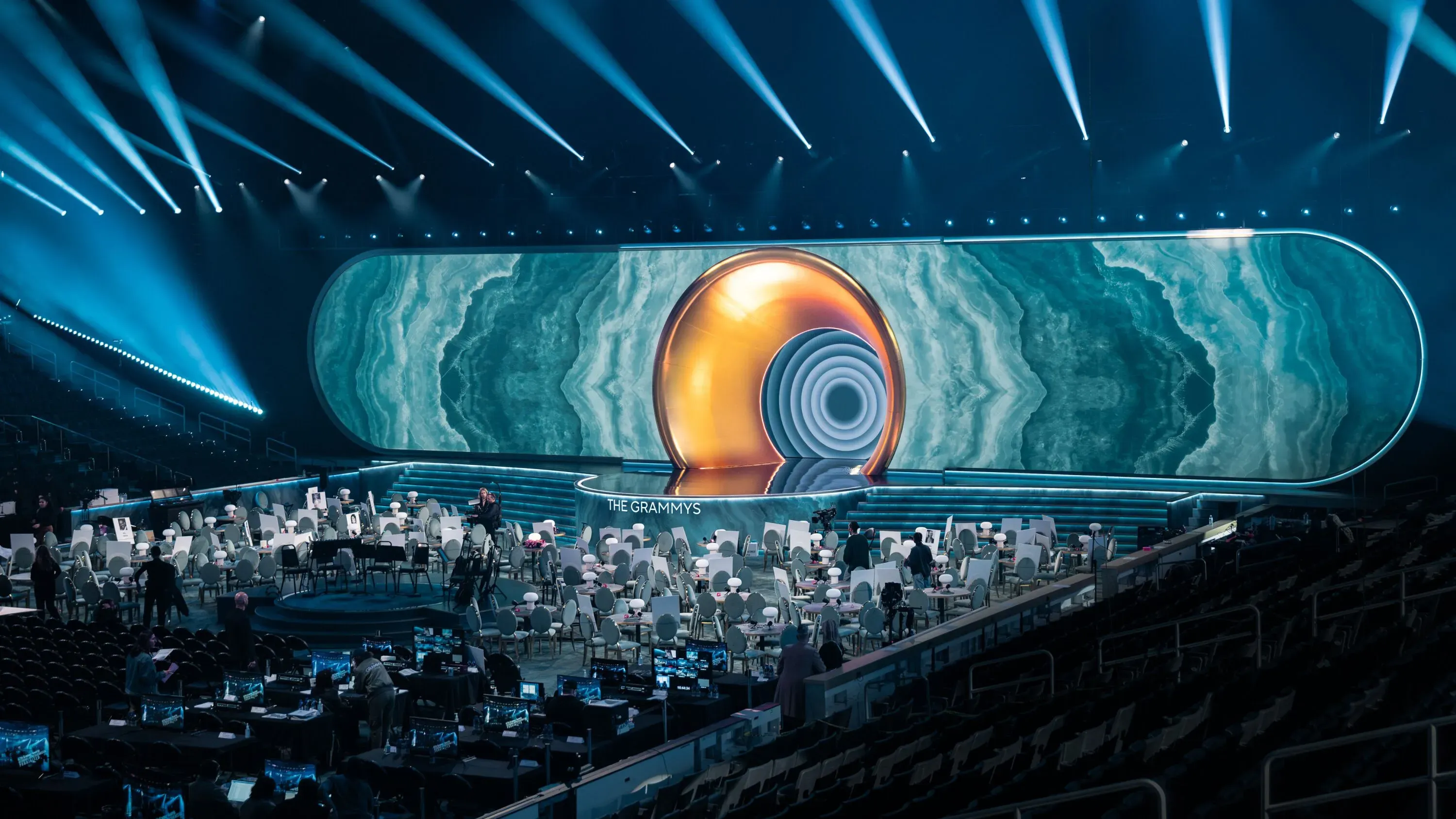 تصميم مسرح حفل توزيع جوائز غرامي مع إضاءة زرقاء وأضواء ساطعة، حيث تظهر الكراسي الفارغة في الخلفية، مما يعكس أجواء الاستعدادات للحدث.