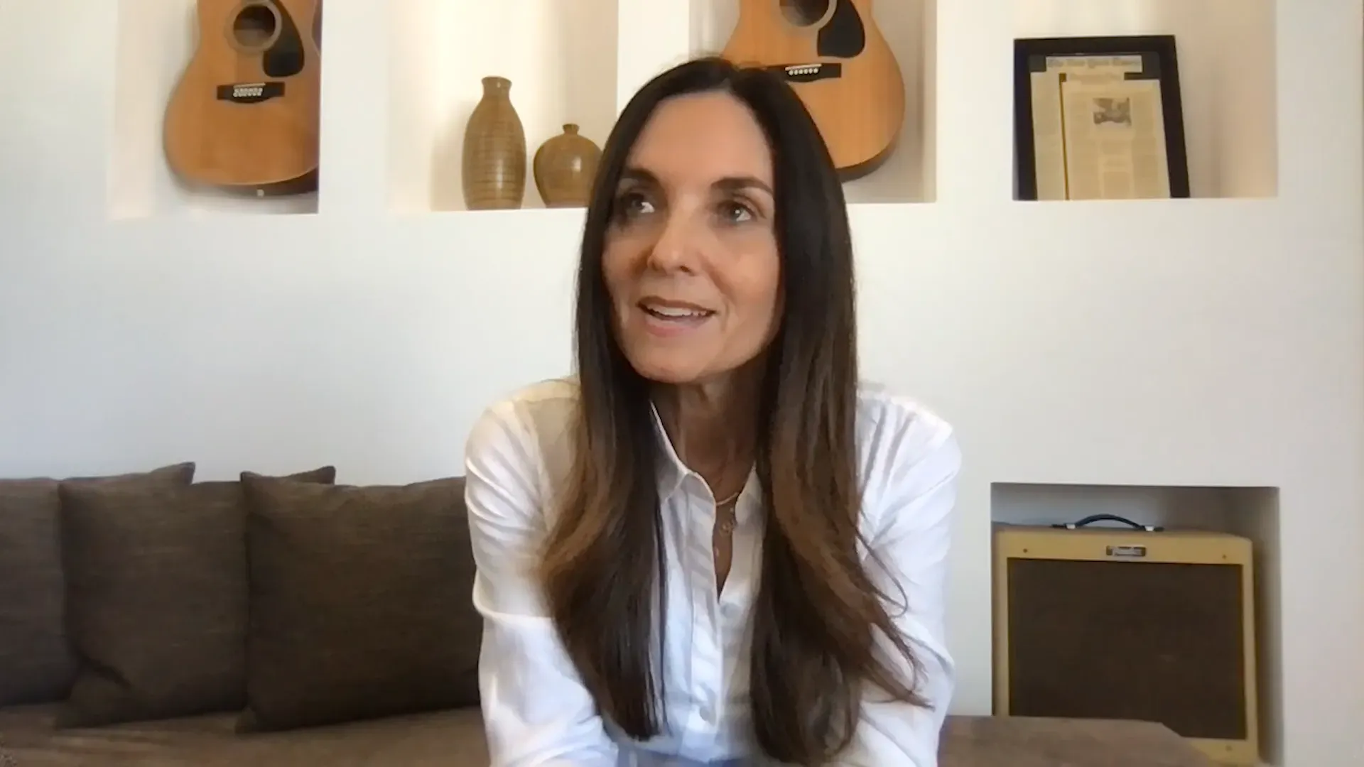 نيكول ساكس تتحدث في مقابلة حول تأثير الألم المزمن وعلاج طب العقل والجسم. تظهر خلفها أدوات موسيقية وديكور داخلي.