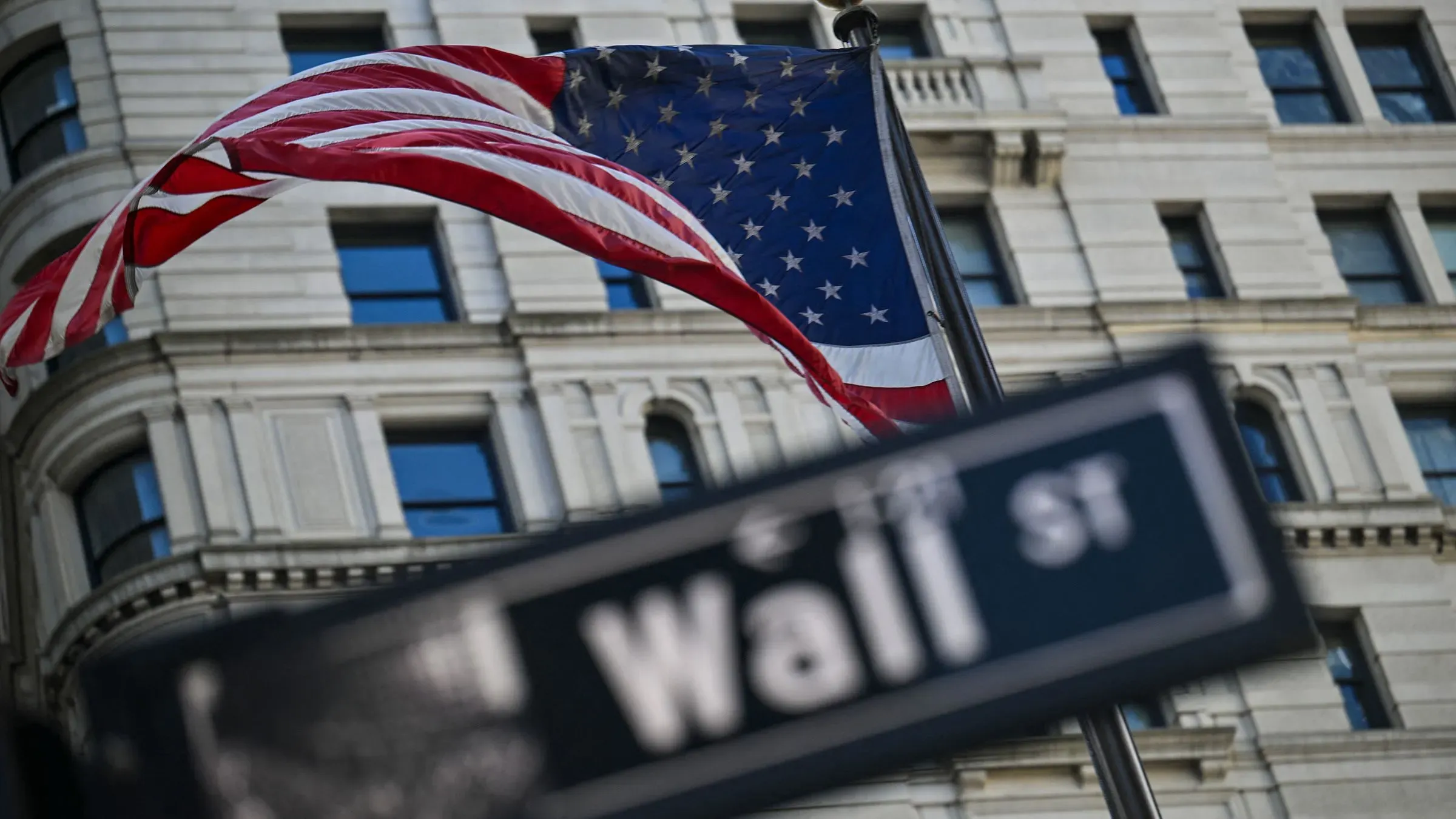علم الولايات المتحدة يرفرف أمام مبنى في وول ستريت، رمز الأسواق المالية الأمريكية، وسط تراجع الأسهم بسبب الرسوم الجمركية.