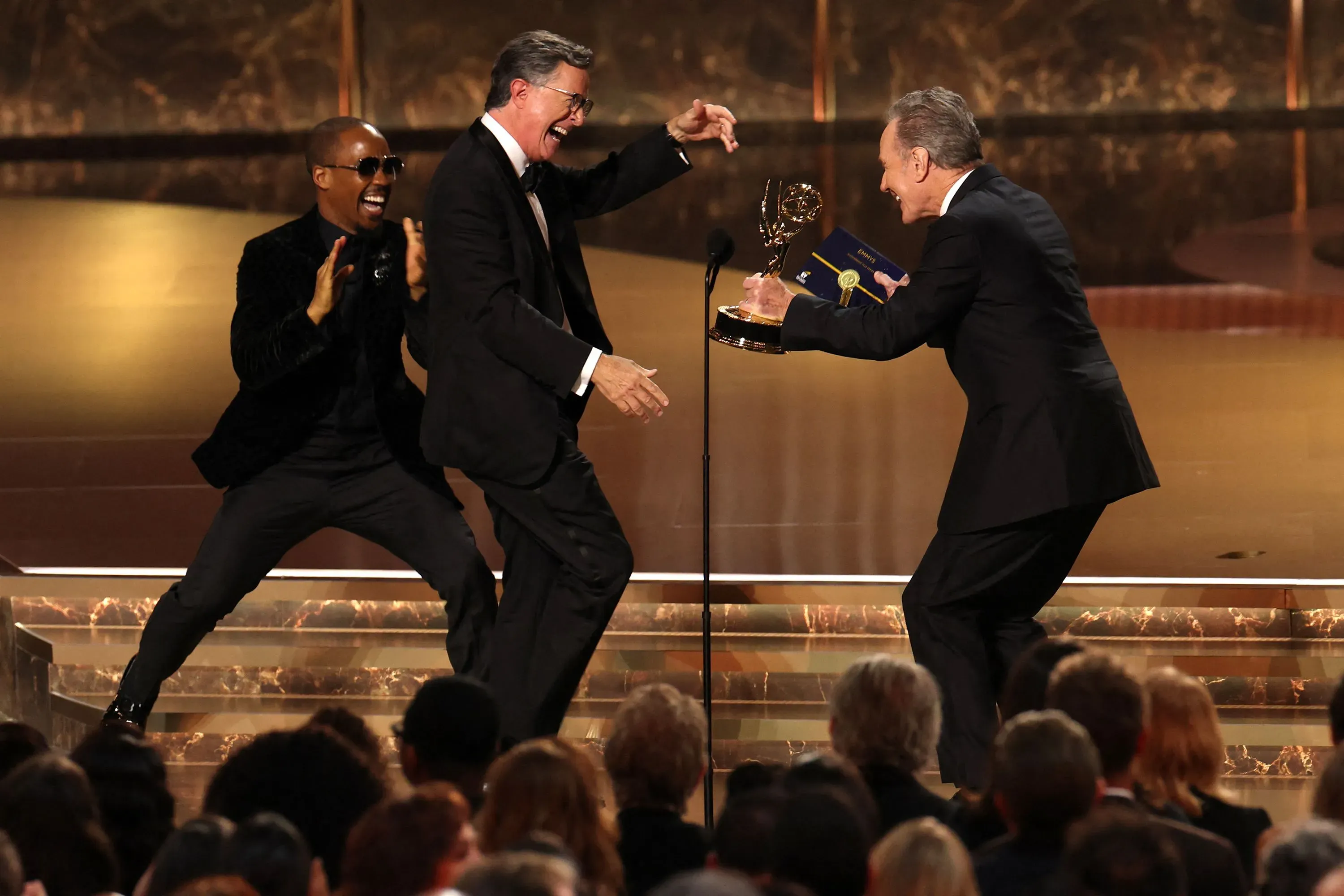 لحظة احتفالية في حفل جوائز إيمي 2025، حيث يتلقى ستيفن كولبير جائزة إيمي وسط تصفيق حار من الجمهور.