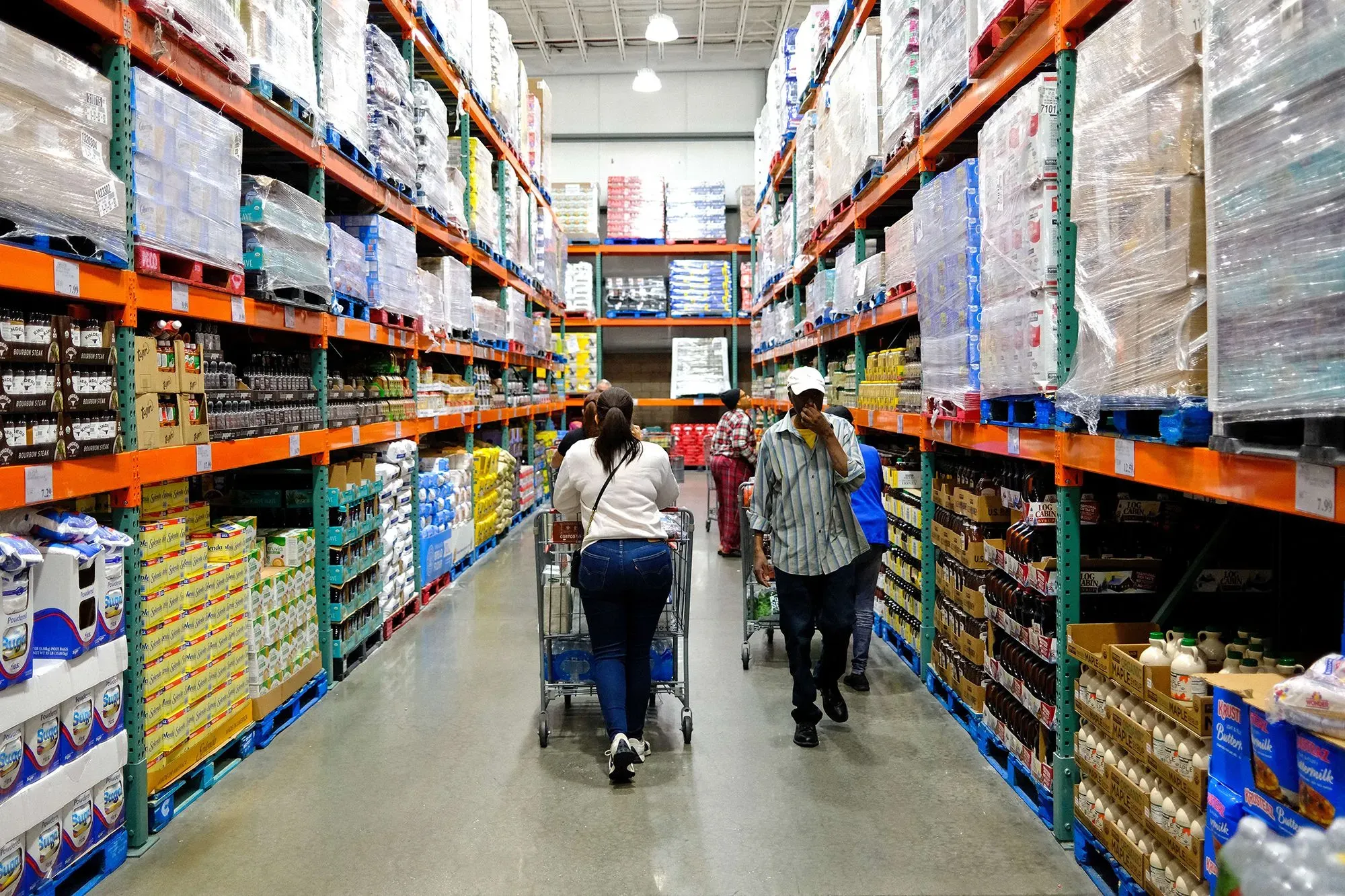 متسوقون يتجولون في ممرات متجر كبير، محاطون بأرفف مليئة بالسلع المتنوعة، مما يعكس تأثير ارتفاع الأسعار على تكلفة المعيشة.