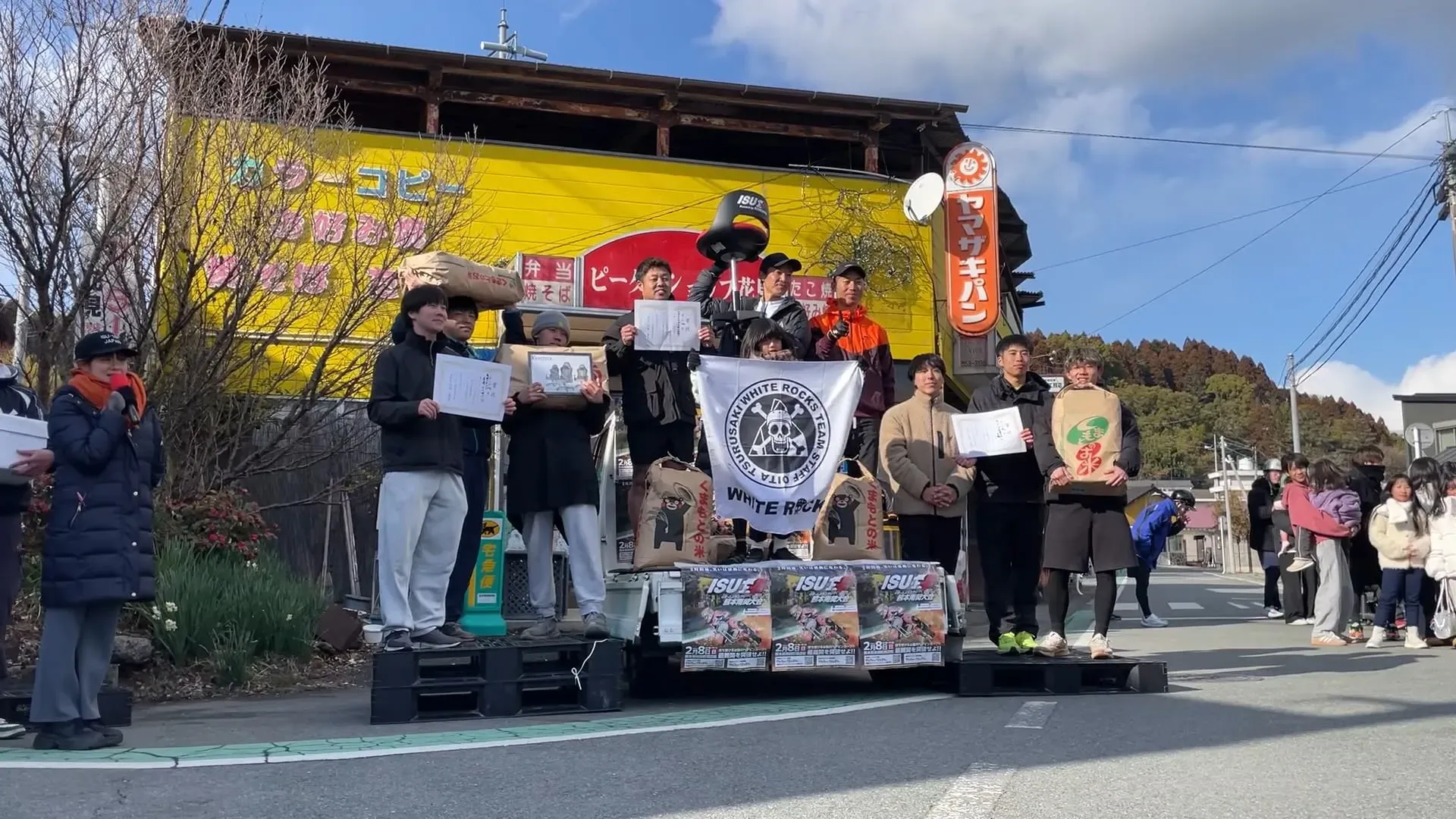 مجموعة من المشاركين في سباق الكراسي المكتبية في أودايبا بطوكيو، يحملون لافتات ويستعدون للتنافس في حدث رياضي فريد.