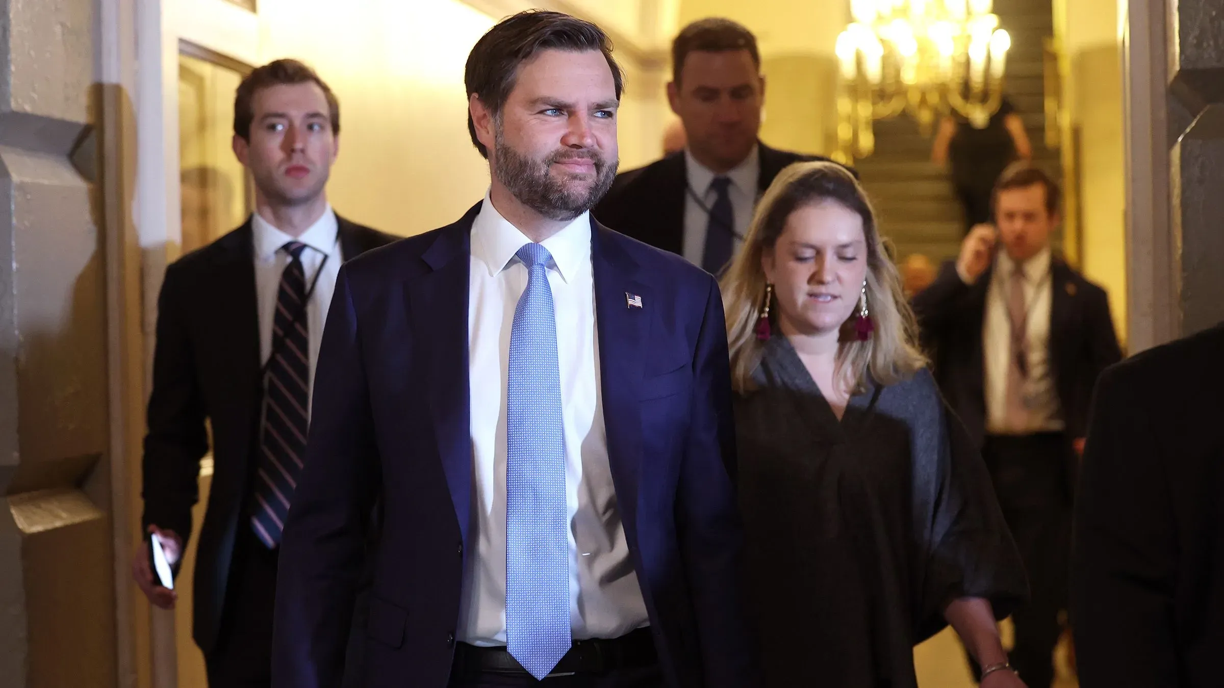 رجل يرتدي بدلة رسمية يسير مع مجموعة من الأشخاص في ممر، يعكس شعور التوتر في السياسة الخارجية الأمريكية تجاه أوروبا.